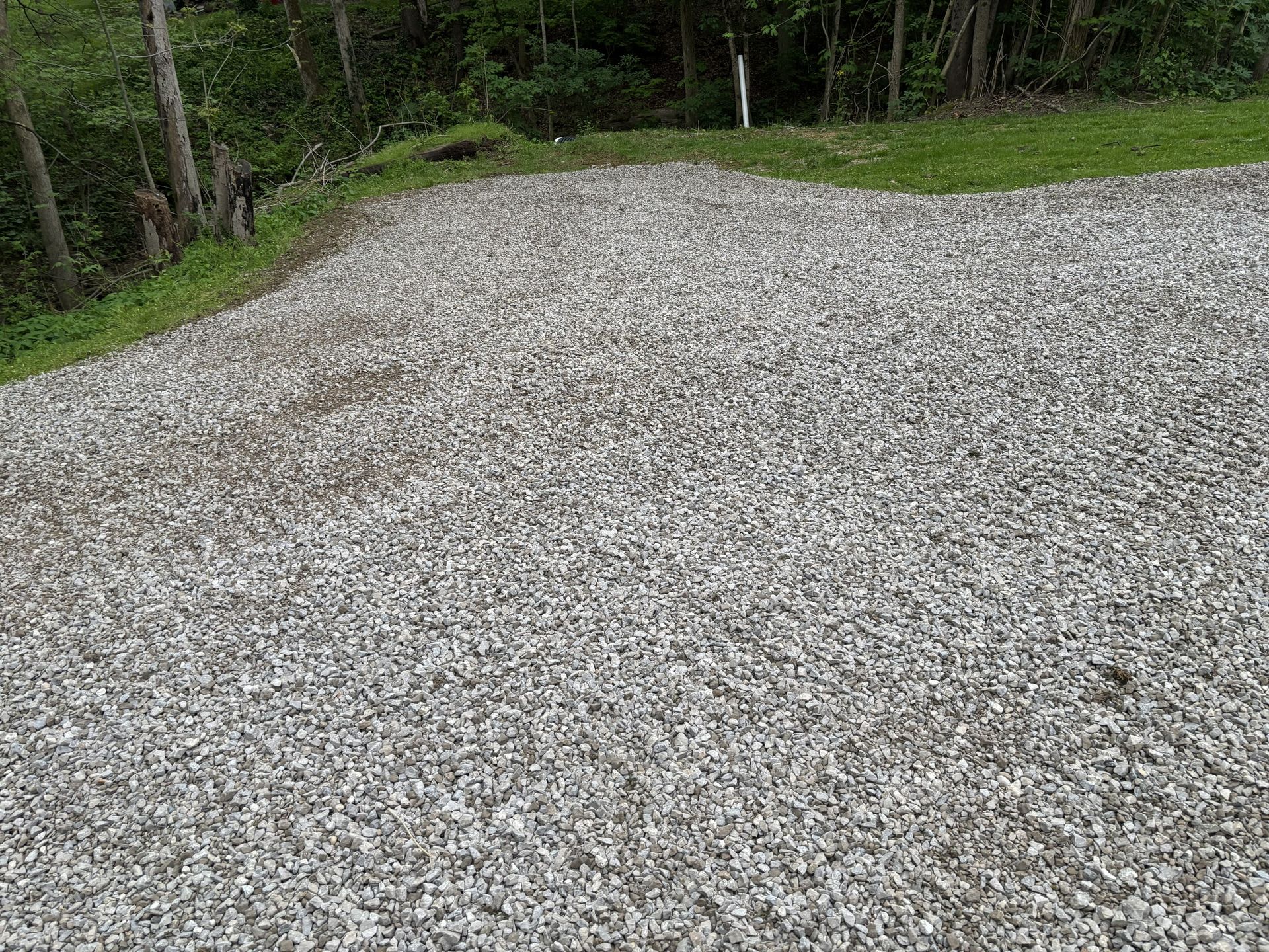 Gravel driveway or parking area bordered by grass and trees on a cloudy day