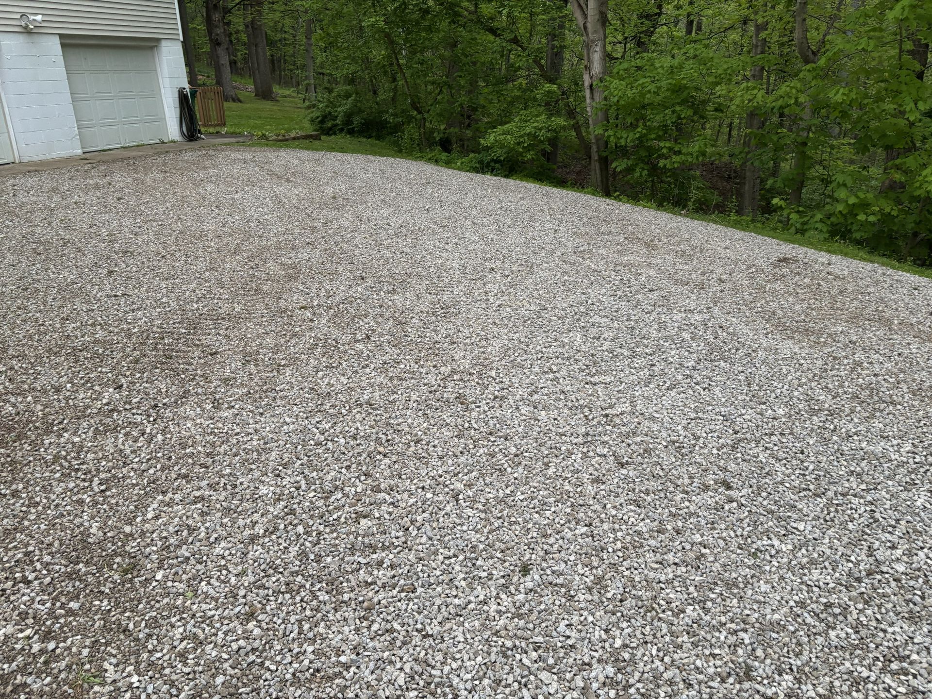 Gravel driveway beside a garage, with trees and a wooded slope in the background.