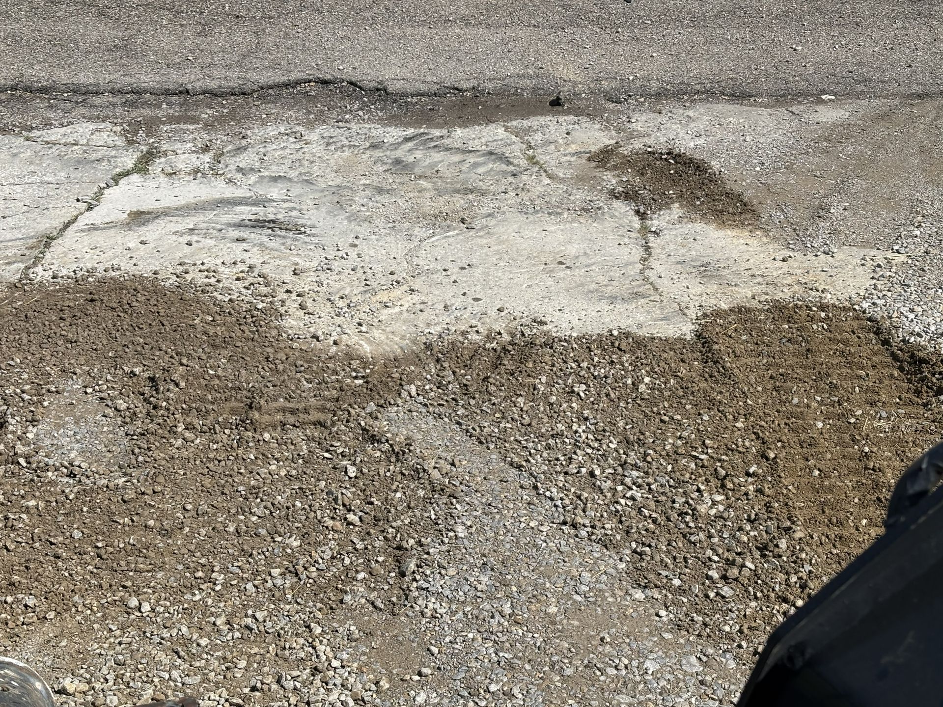 Gravel ground with a large white concrete patch and a dark object at the lower right edge