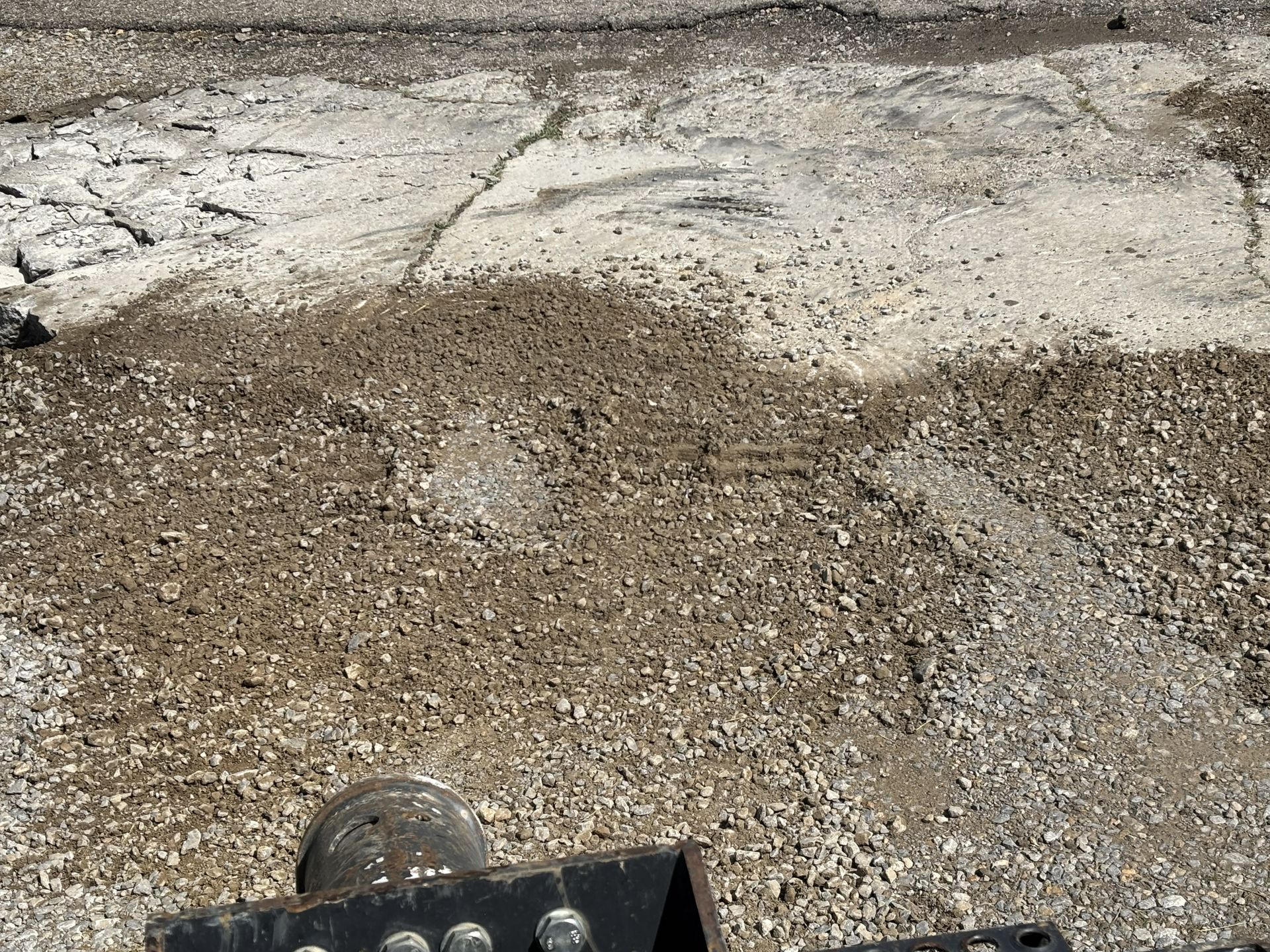 Rocky, gravelly ground with a concrete edge and a small black object at the bottom.