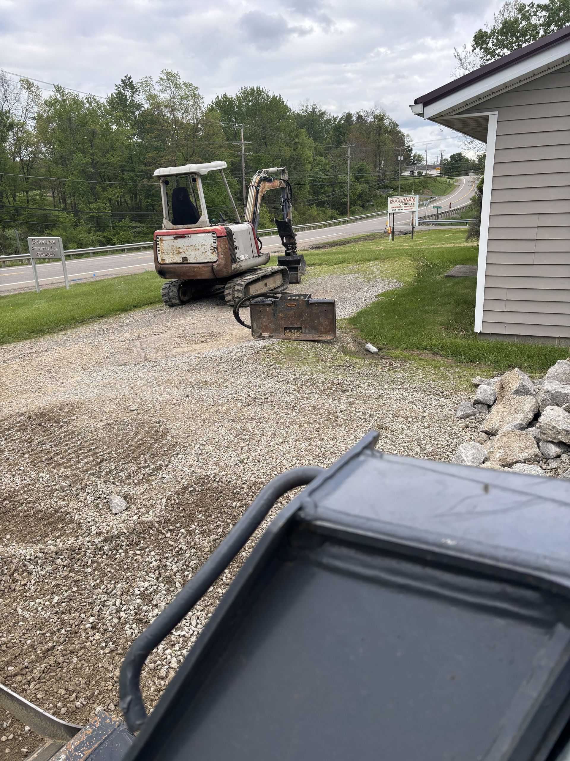 Small excavator digging gravel beside a white house on a rural driveway