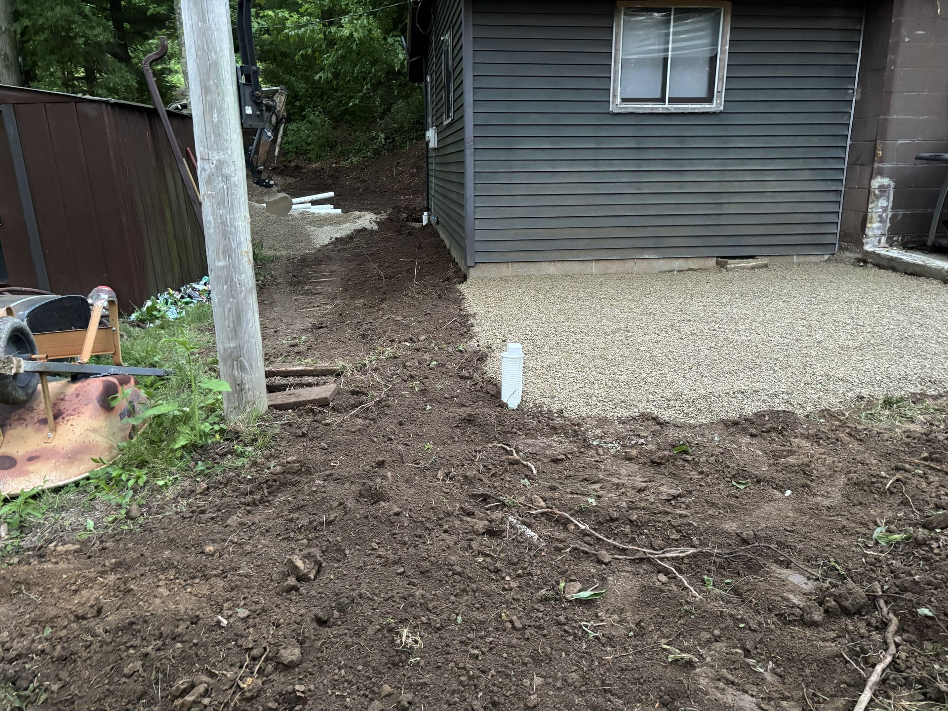 Backyard with a dirt trench, gravel area, utility pole, and gray shed near a fence.