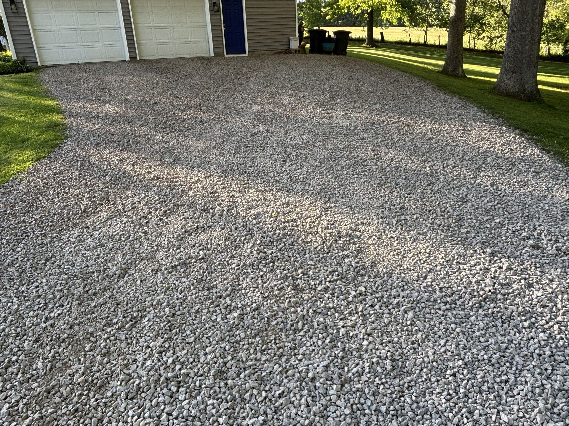 Gravel driveway beside a house and trees in a sunny yard.
