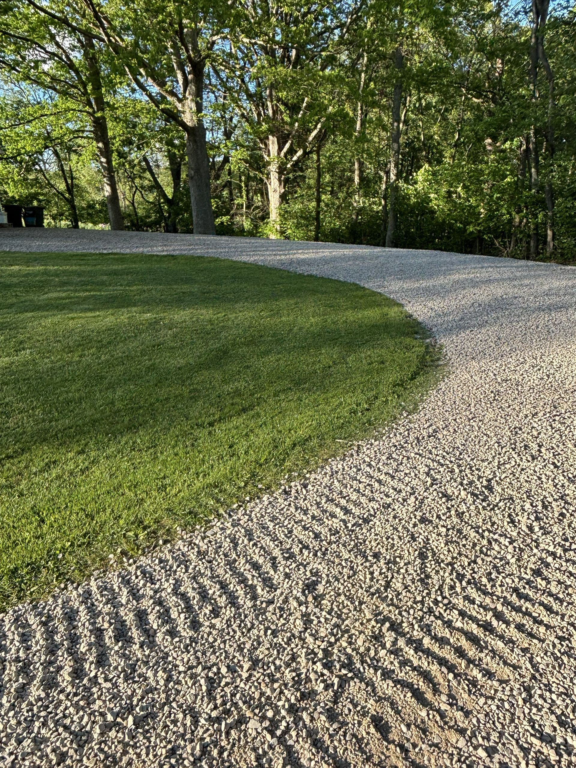 Curving gravel path beside a grassy hill in a wooded park at sunset
