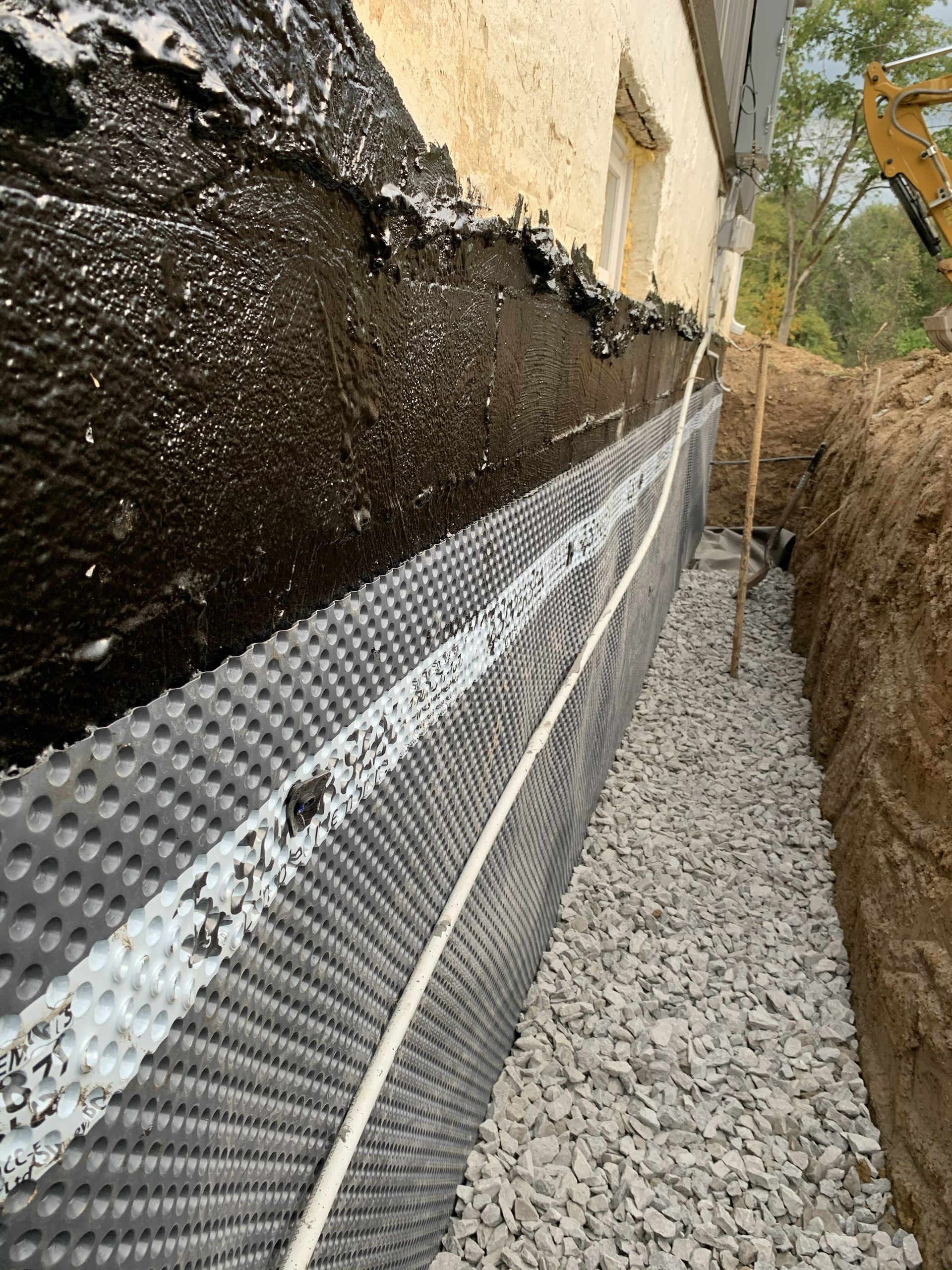Gravel-filled trench with a drainage membrane along a foundation wall outdoors