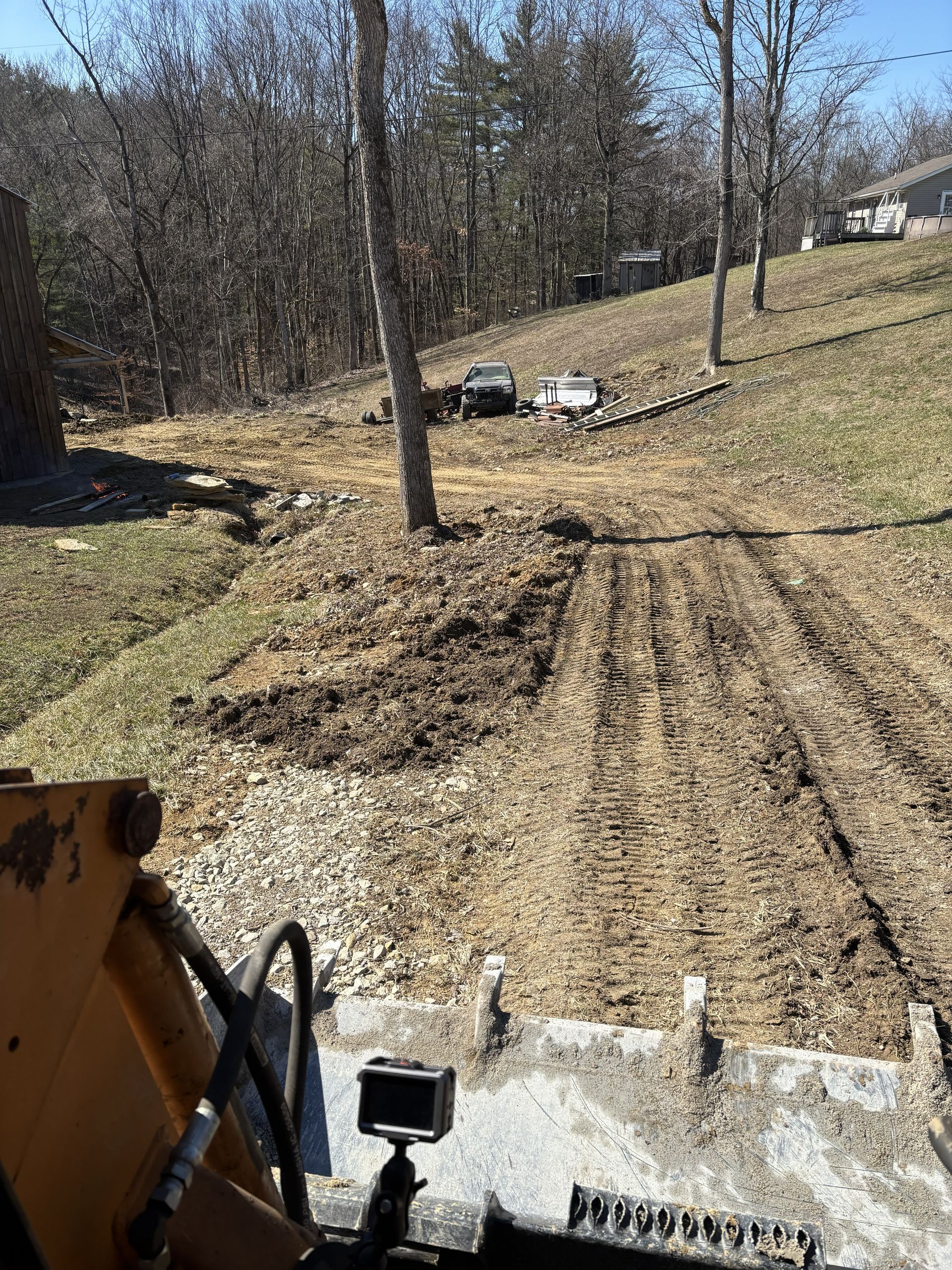 ATV view of a muddy, rutted dirt path on a wooded hillside with parked vehicles ahead.