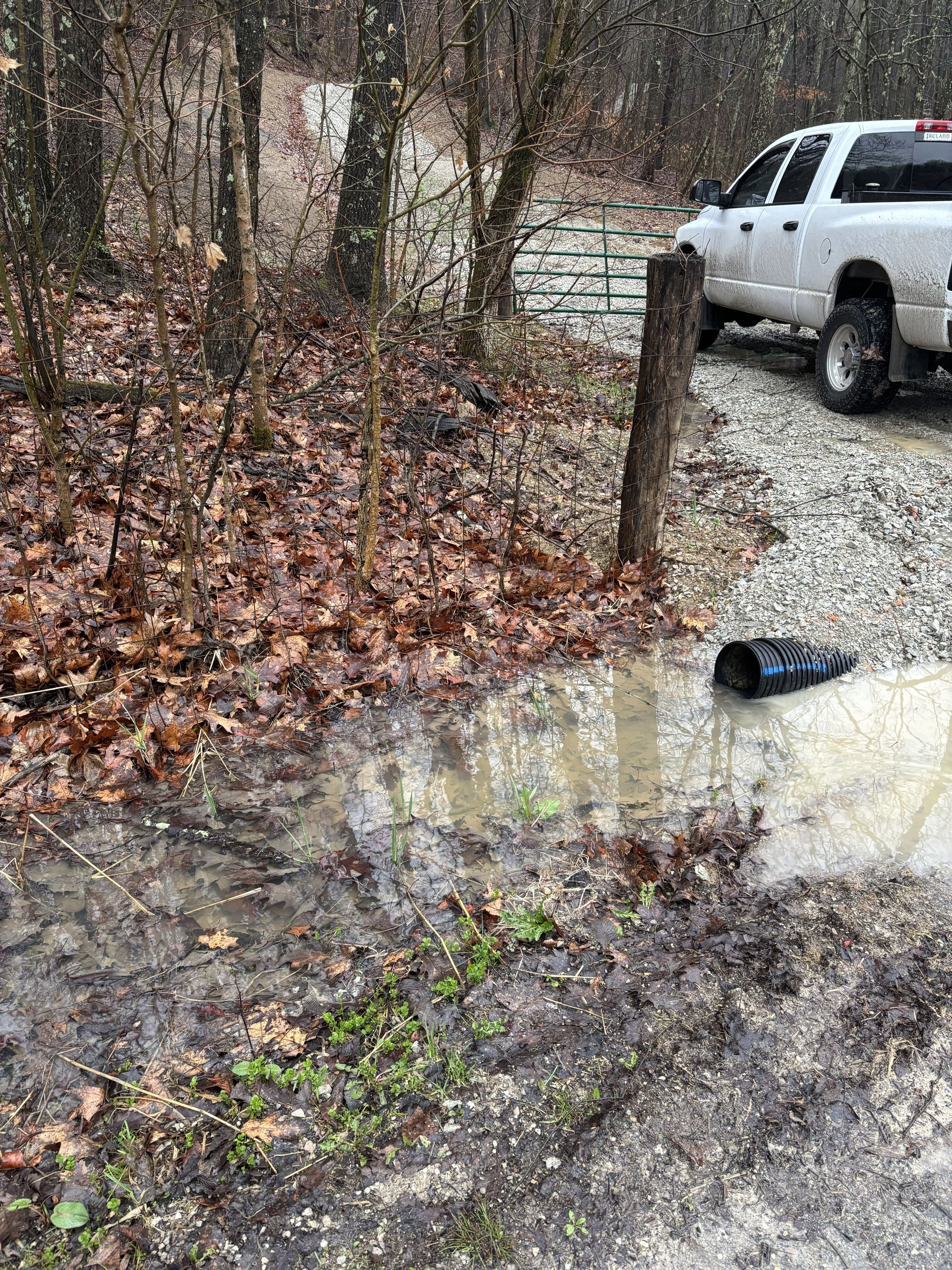Snowy gravel driveway with muddy puddles, a white pickup truck, and a shoe lying near a post.