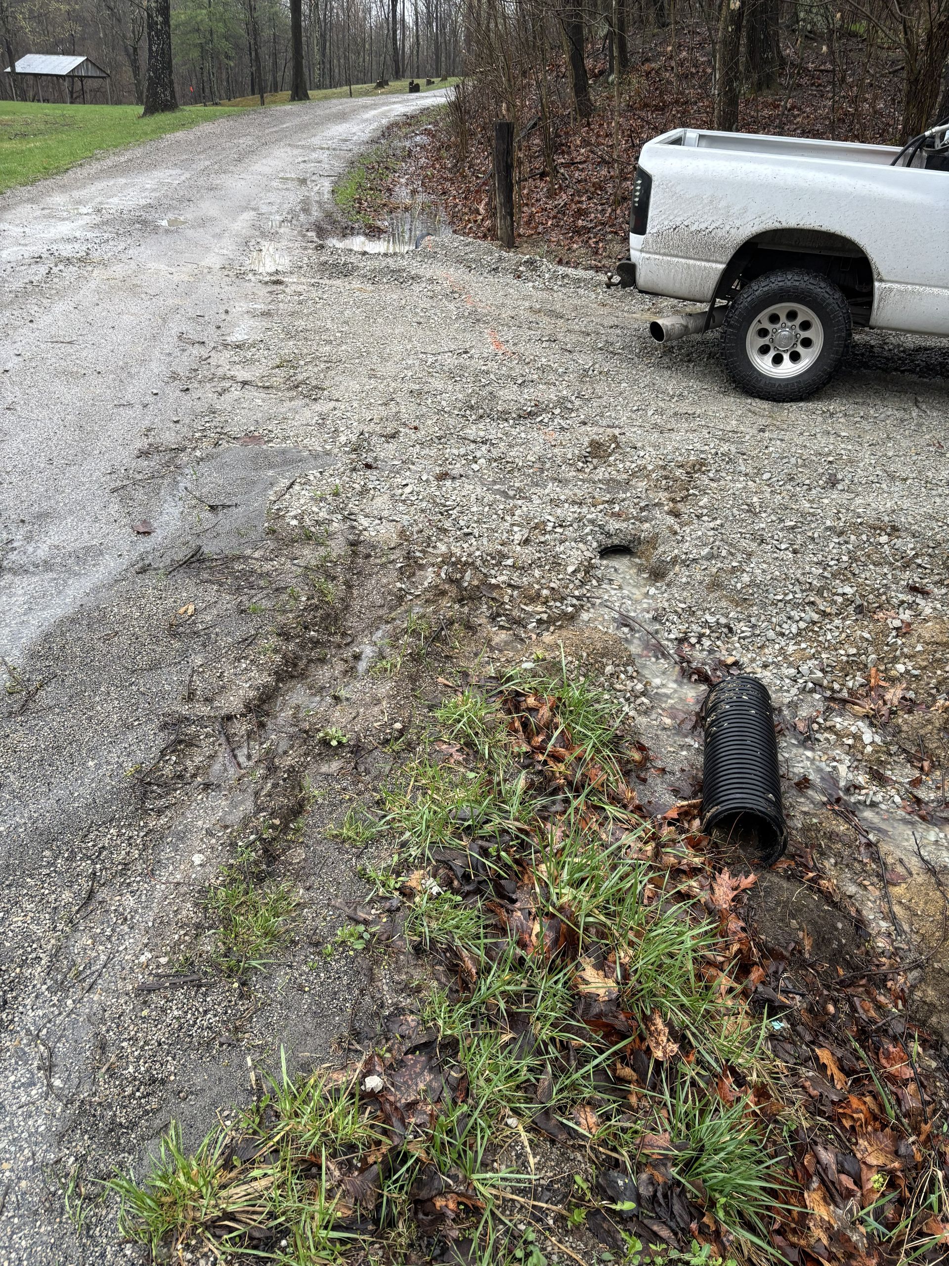 Gravel road on a rainy day beside a white pickup truck and a black fire hydrant.