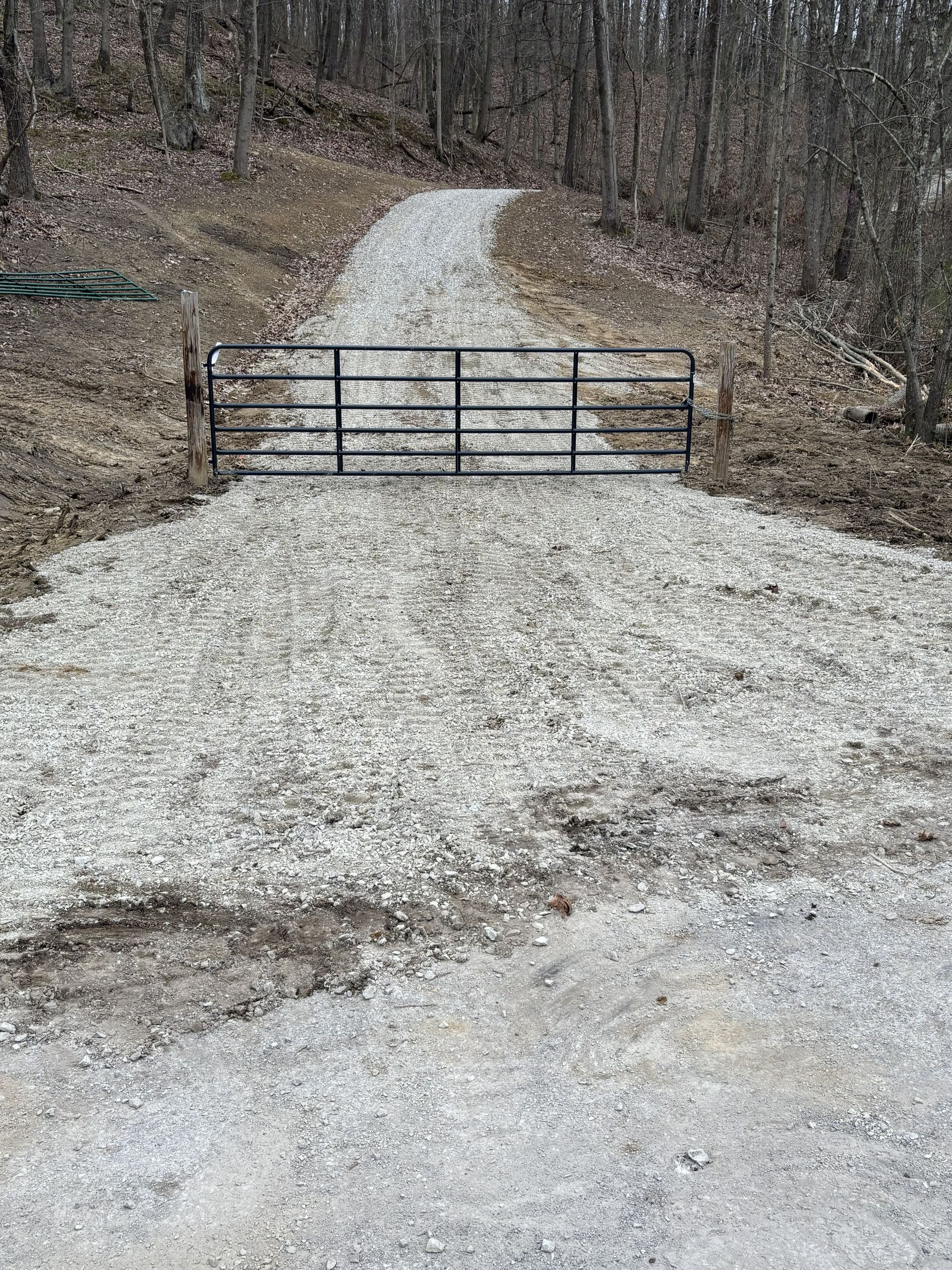 Gravel driveway blocked by a closed metal gate in a wooded area