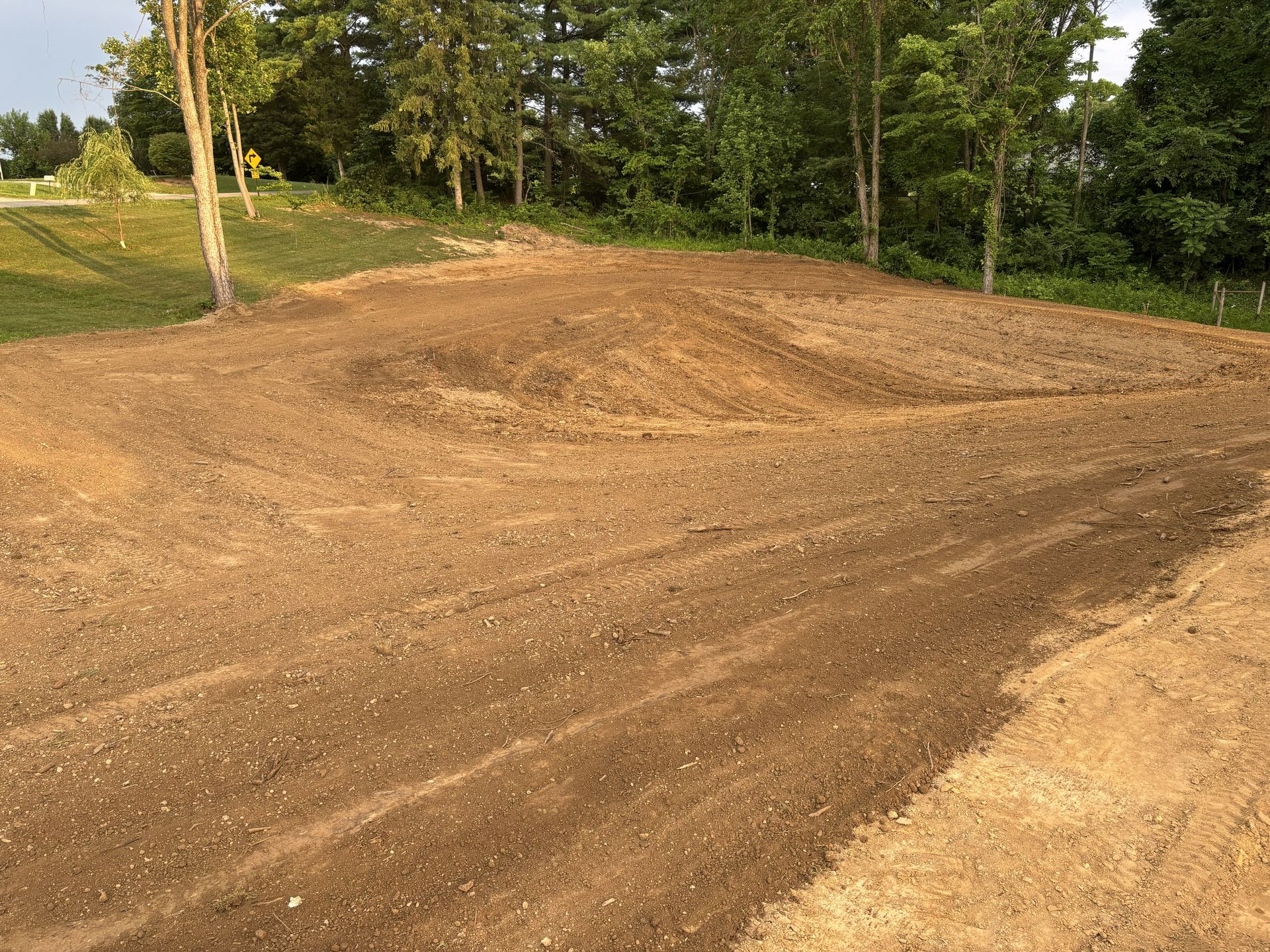 Freshly graded dirt mound beside a dirt road, with trees and grass in the background