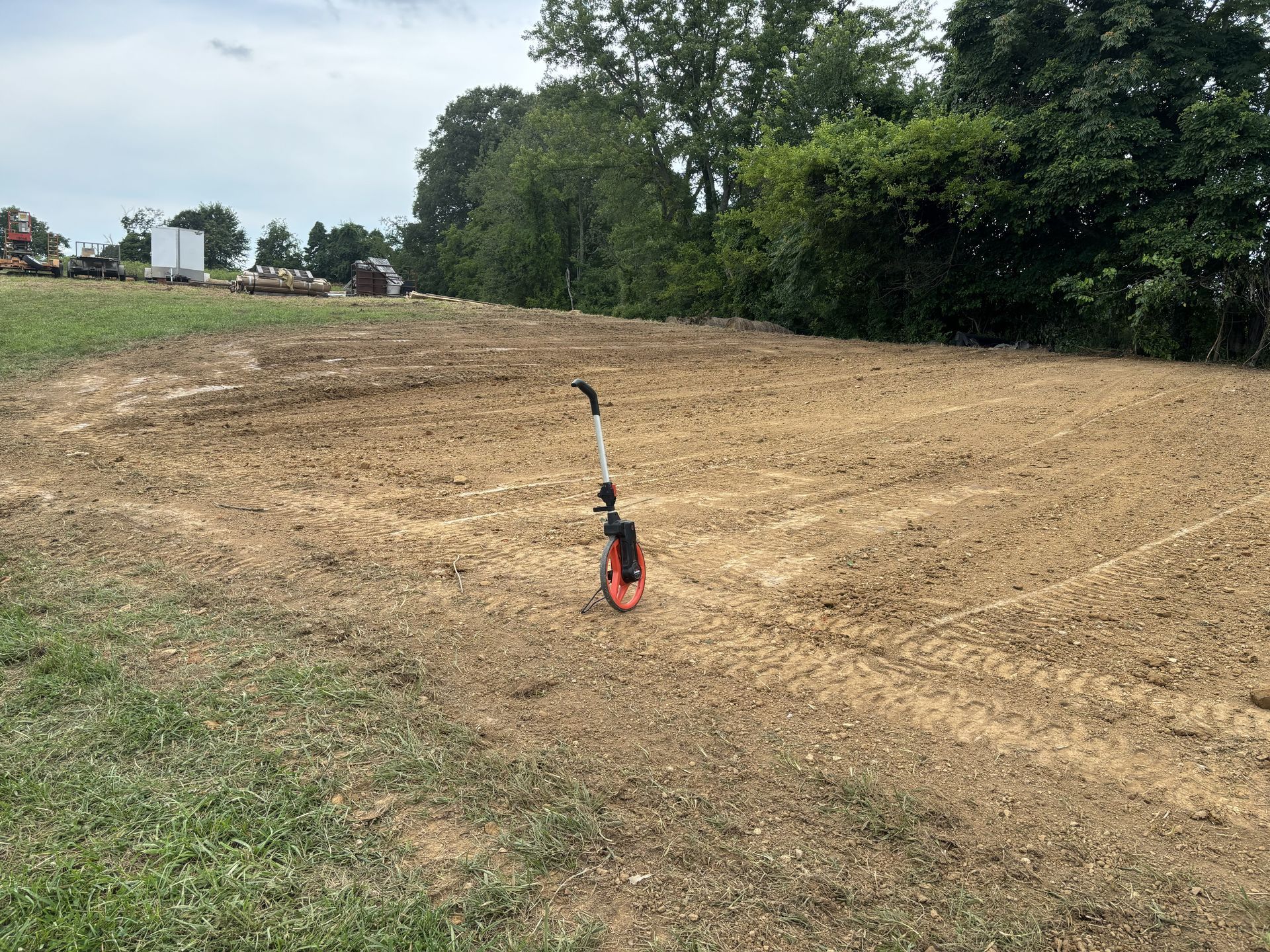 Small red-and-black gas trimmer standing in a freshly cleared field near trees and a dirt road