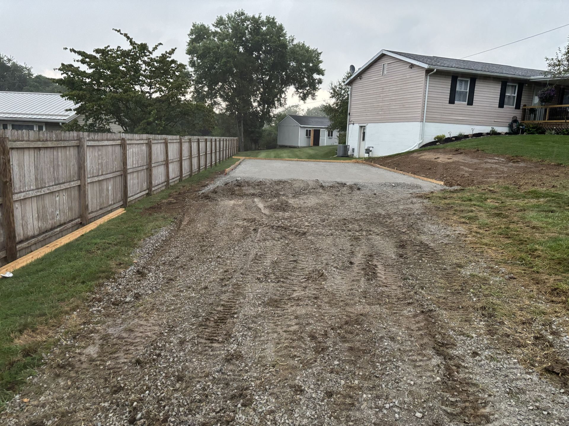 Gravel driveway beside a wooden fence leading to a white house on a grassy slope at dusk