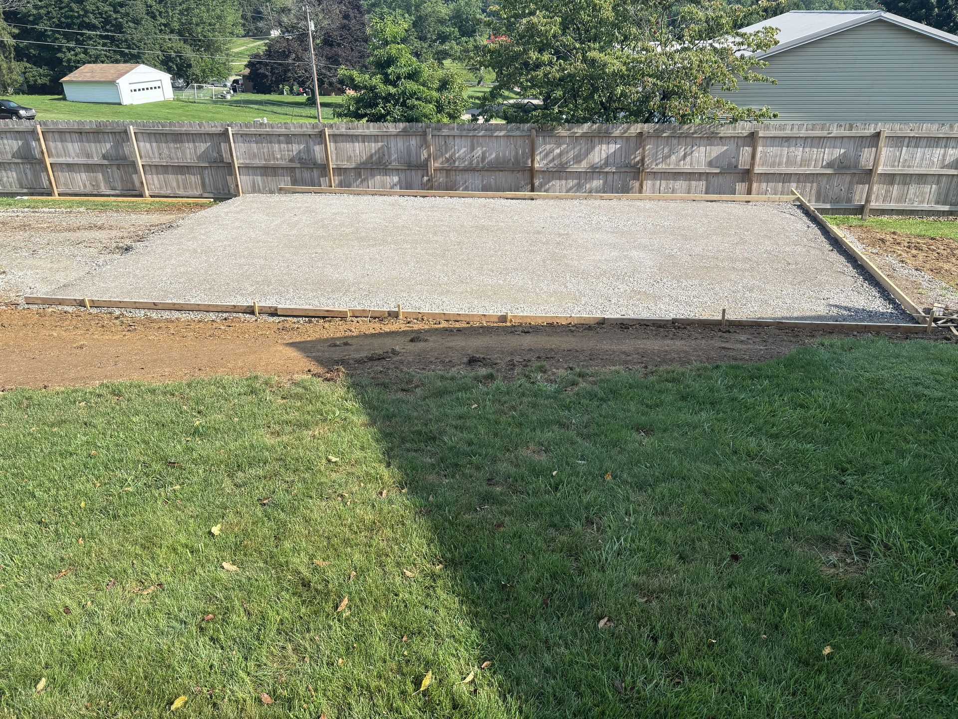 Gravel patio beside a grassy yard, with a wooden fence and house in the background.