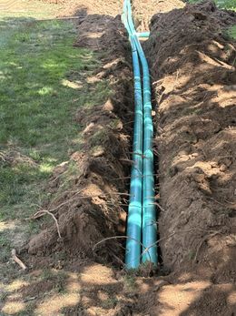 Trenched blue pipes laid side by side beside a dirt mound in a grassy yard