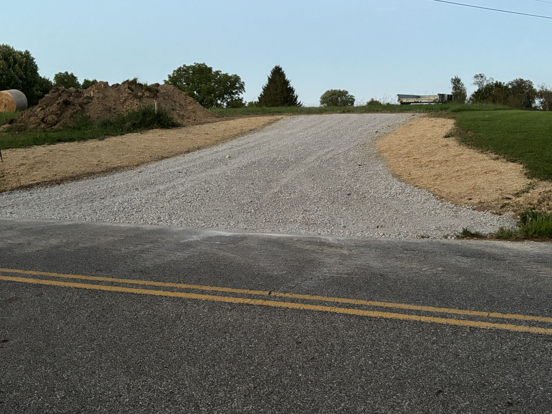 Gravel driveway entrance curving uphill from a paved road in a rural grassy area