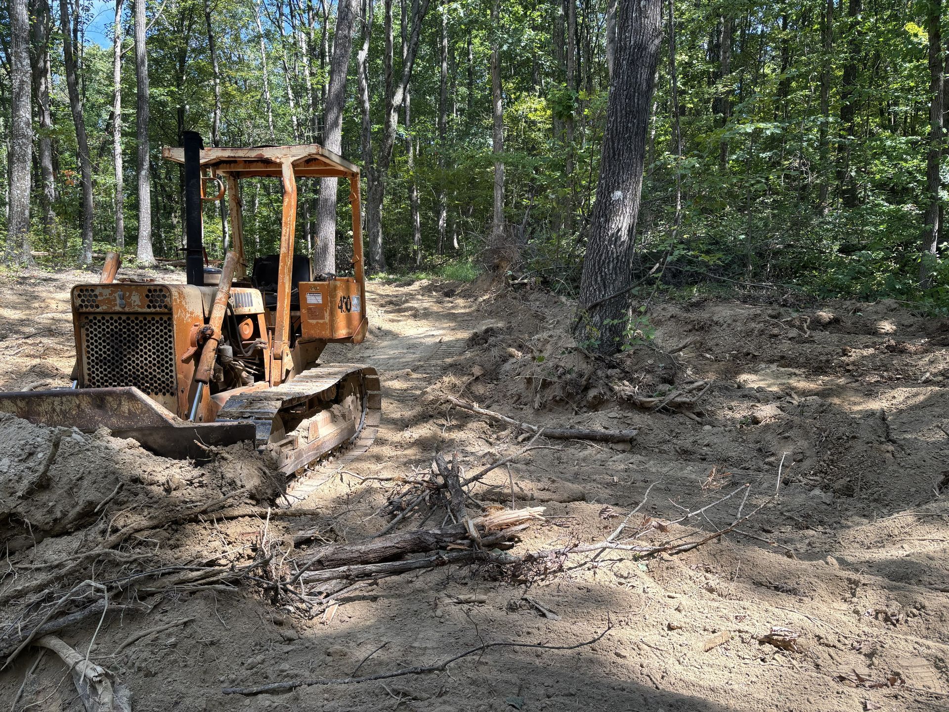 Orange bulldozer grading dirt in a wooded clearing with trees around it