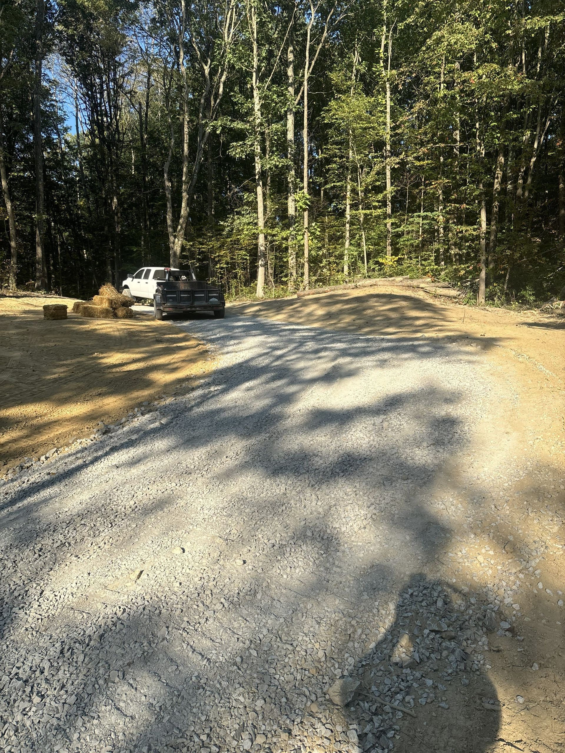 Gravel road curving through a wooded area, with a parked white truck on the left.