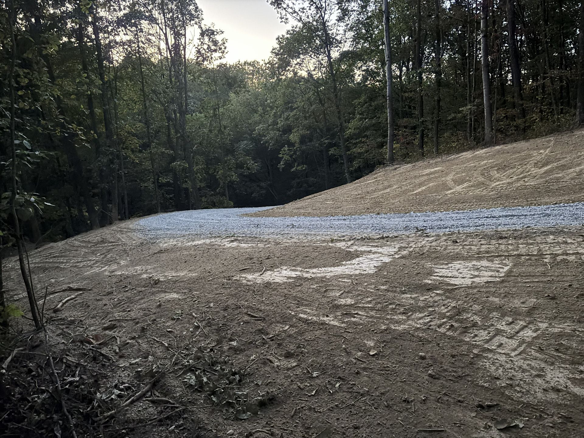 Gravel drive cutting through a wooded hillside at dusk