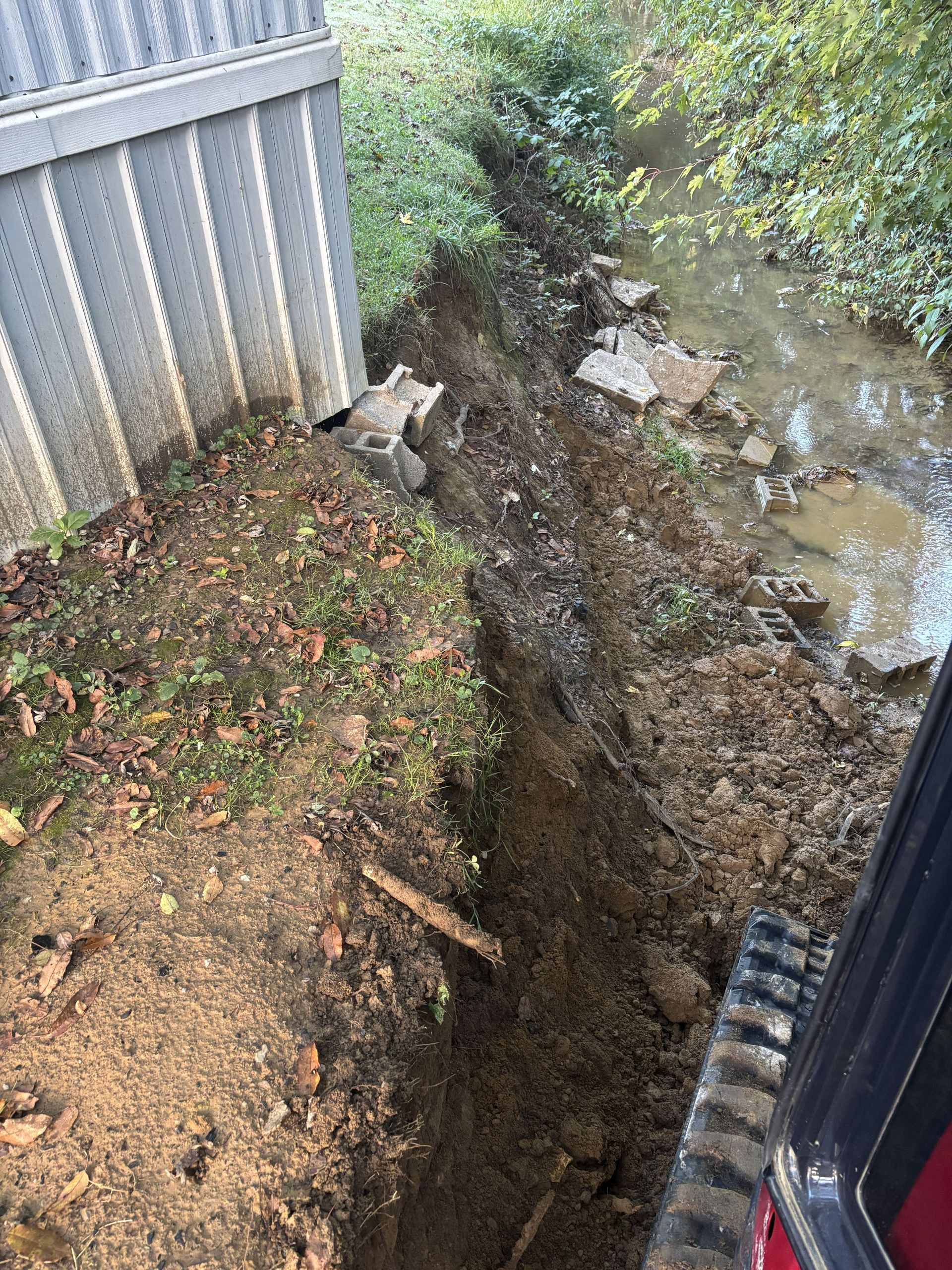 Collapsed ground beside a fence, with a deep muddy erosion trench and standing water.