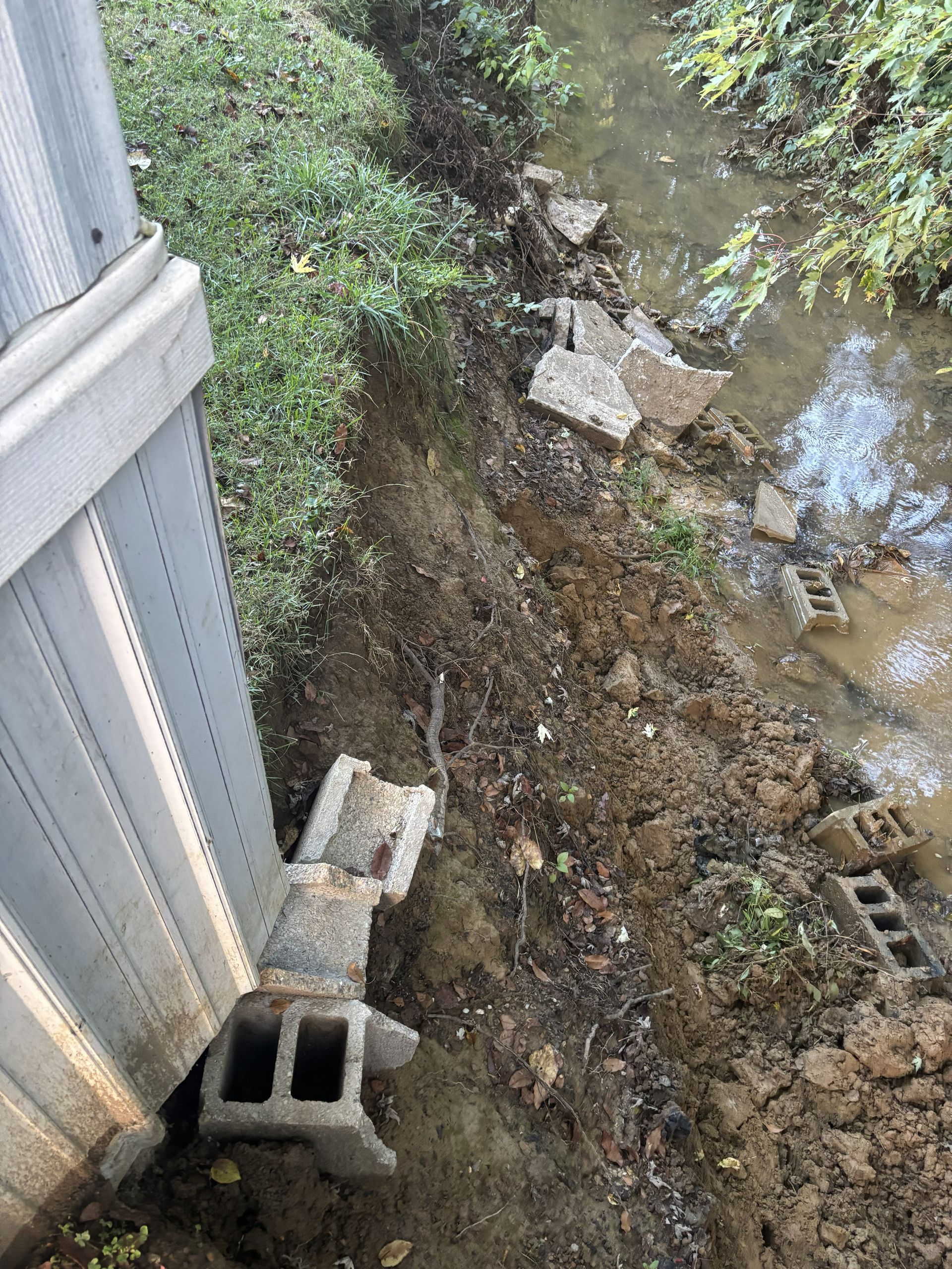 Flooded muddy bank beside a metal fence with scattered concrete blocks and cinder blocks.