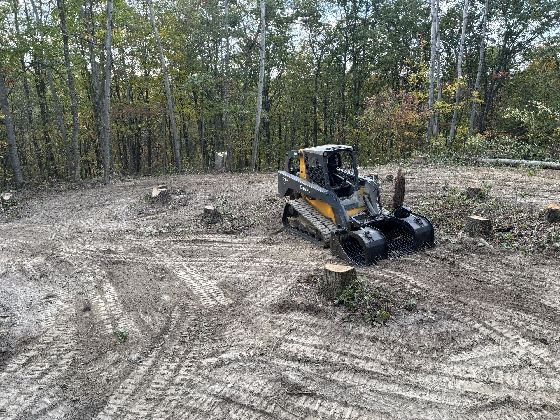 Orange skid steer working on a dirt lot with trees in the background