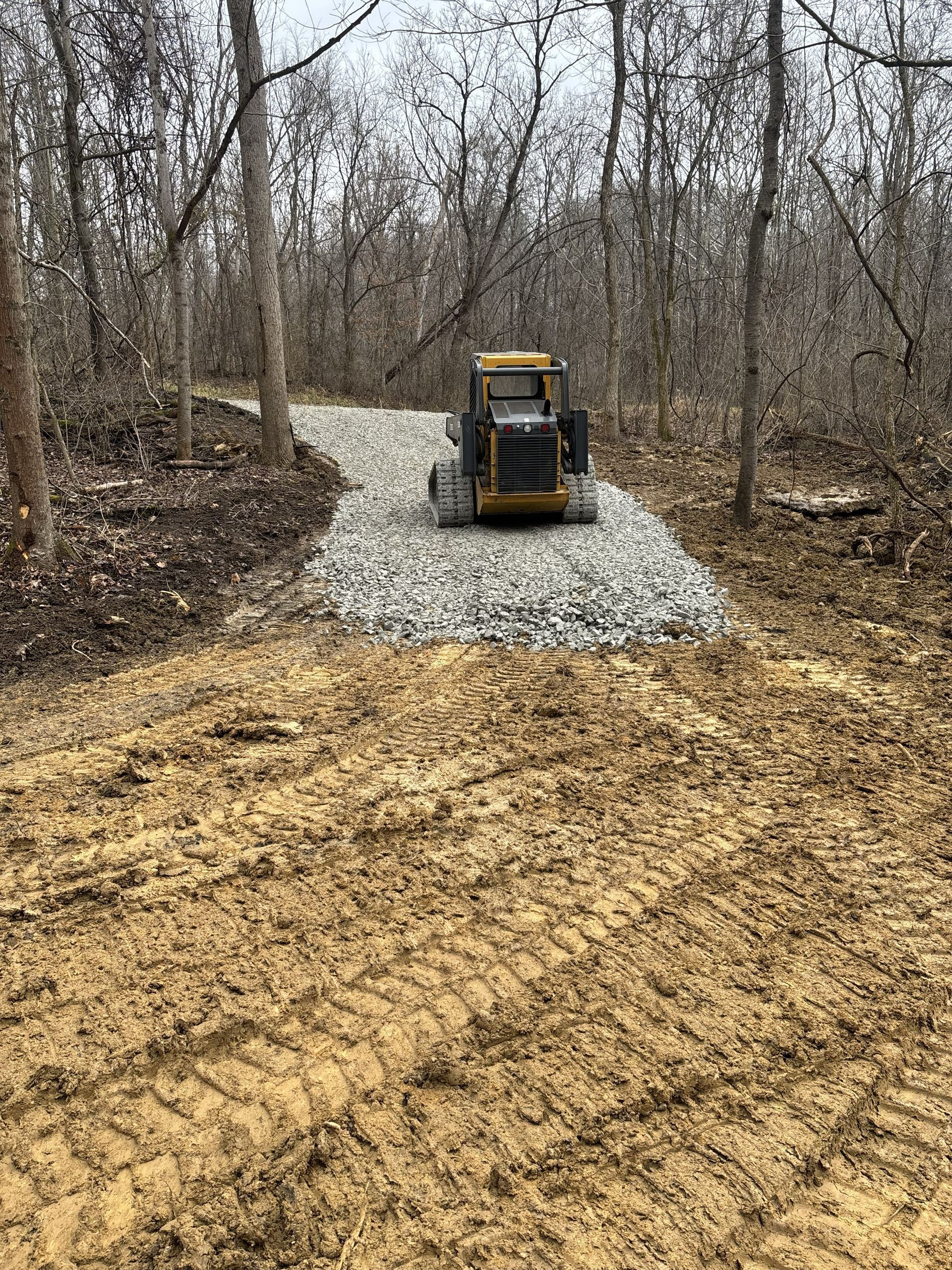 Compact loader on a gravel path in a leafless wooded area