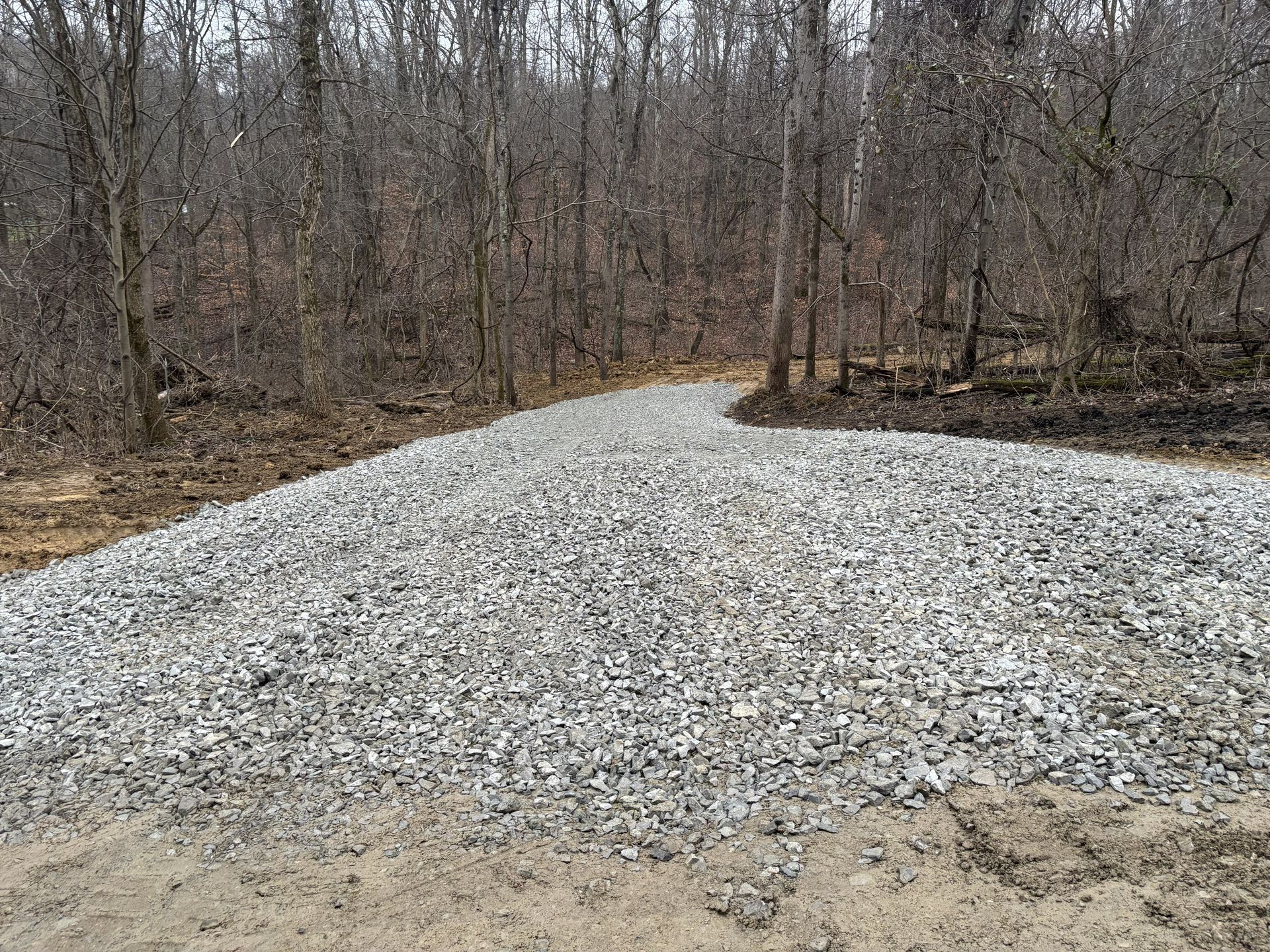 Gravel pile beside a wooded area on a dirt road