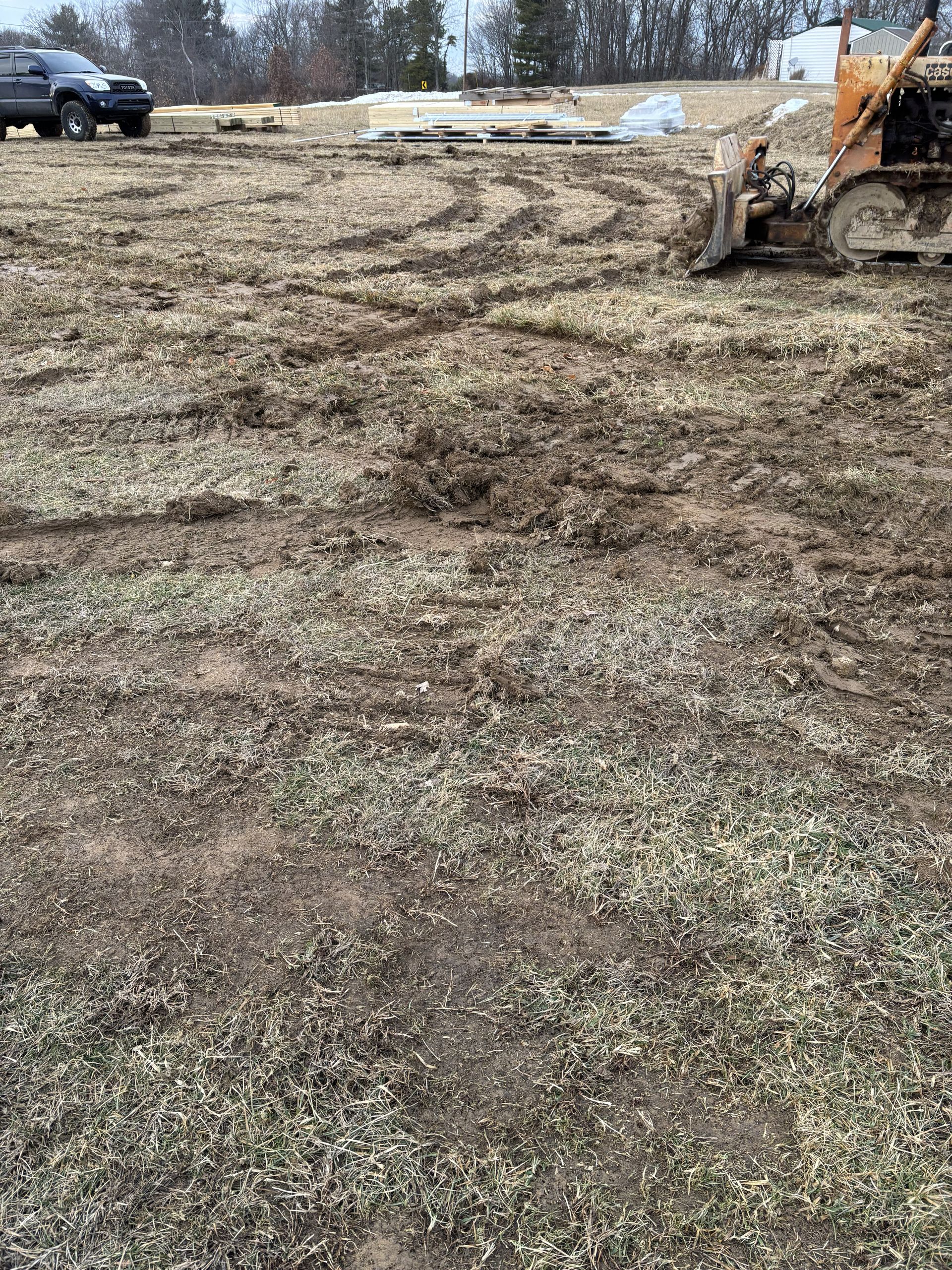 Mud-covered field with a parked truck in the distance and a construction loader at the right edge.