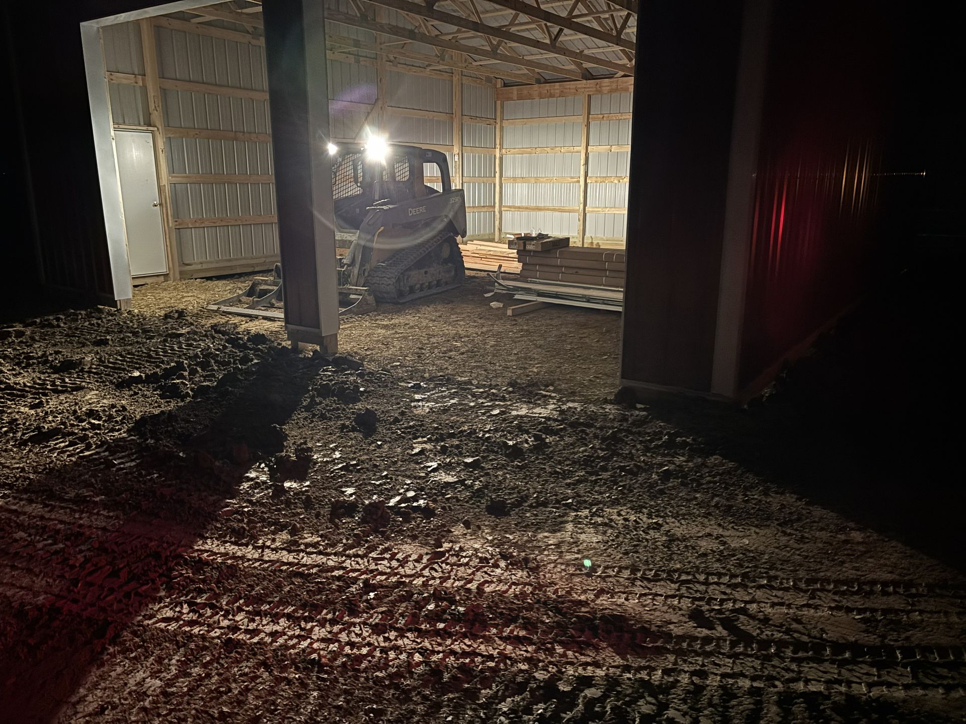 Tractor inside a dimly lit barn with muddy ground and a red light glowing at right