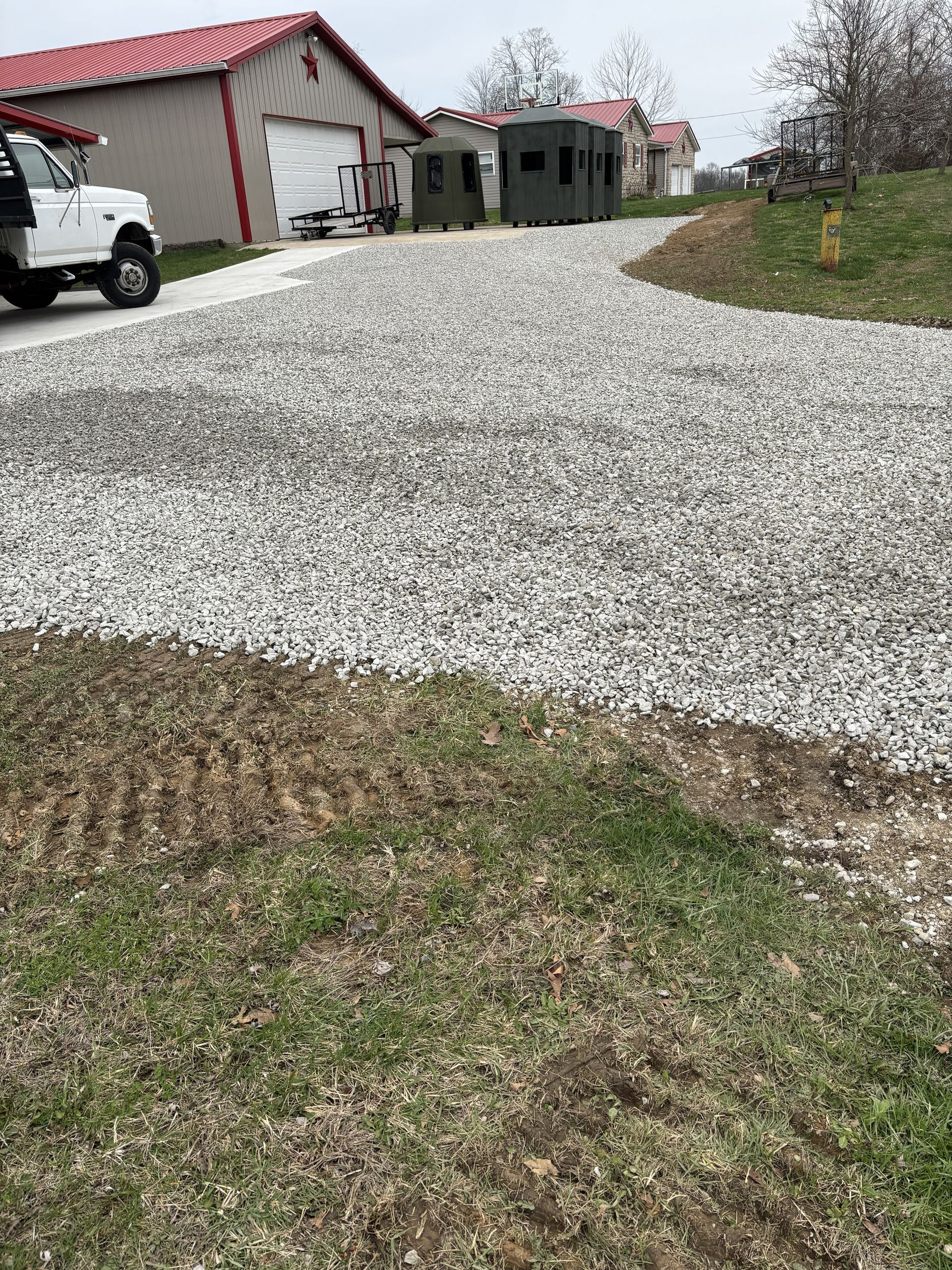 Gravel driveway leading to a house and garage on a cloudy day, with a parked truck on the left.