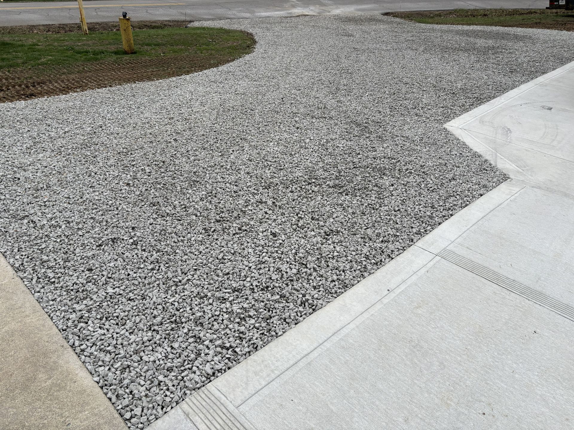 Gravel path beside a light concrete walkway near a grassy area and driveway