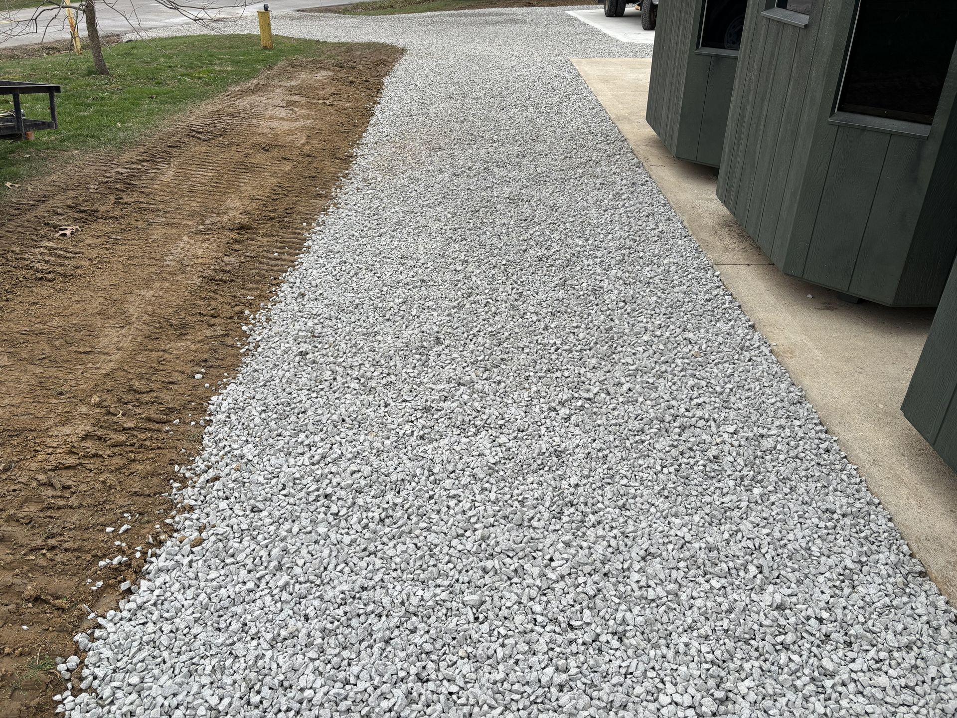 Gravel pathway beside a building, bordered by dirt and grass.