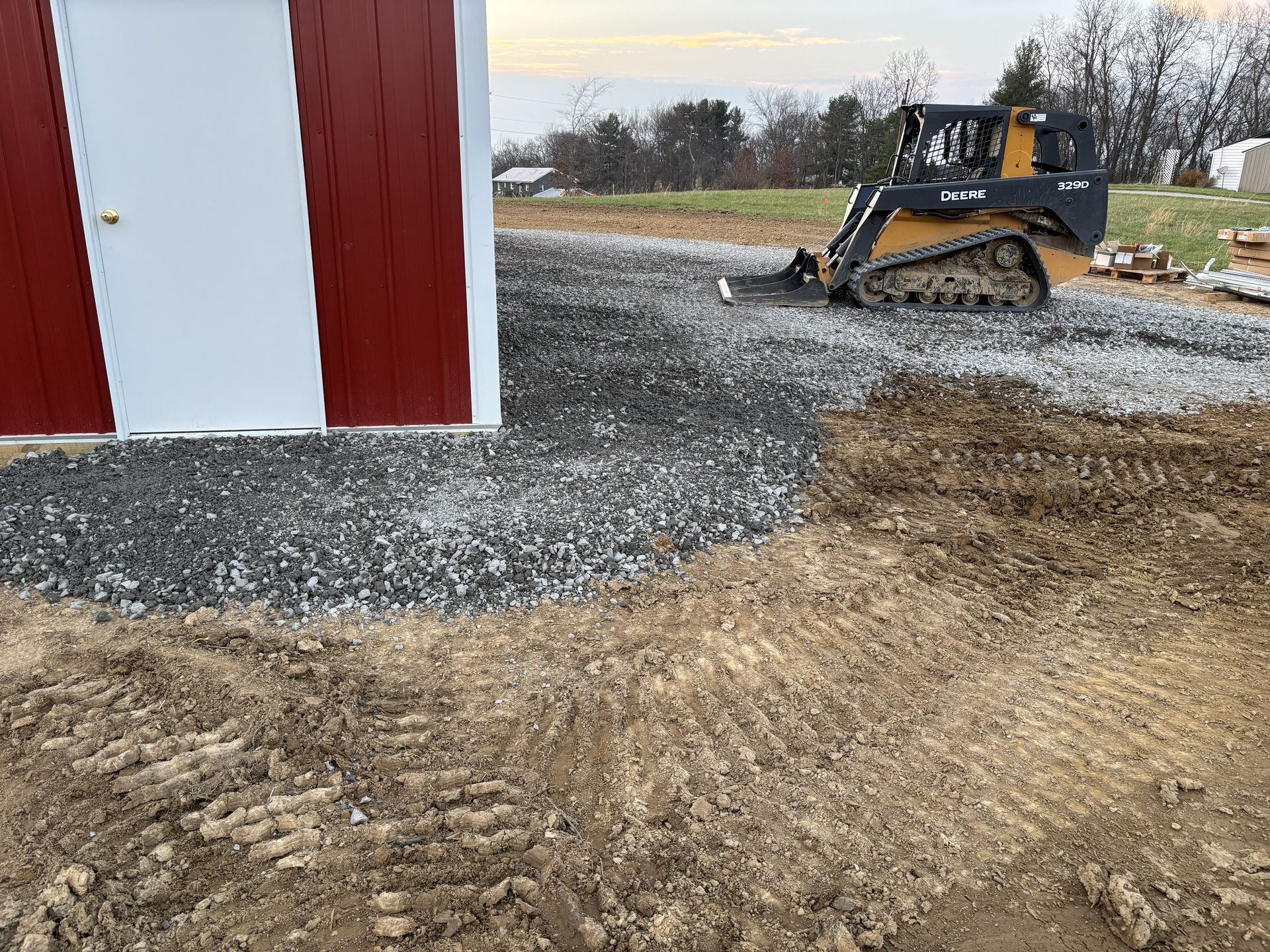 Construction site with a skid steer leveling gravel beside a red-and-white building