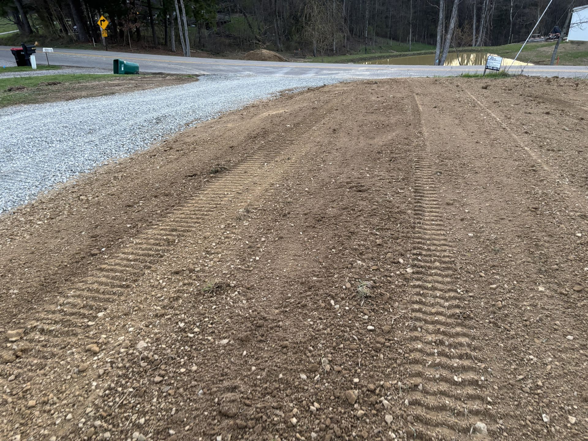 Freshly graded dirt path beside a gravel road in a wooded area