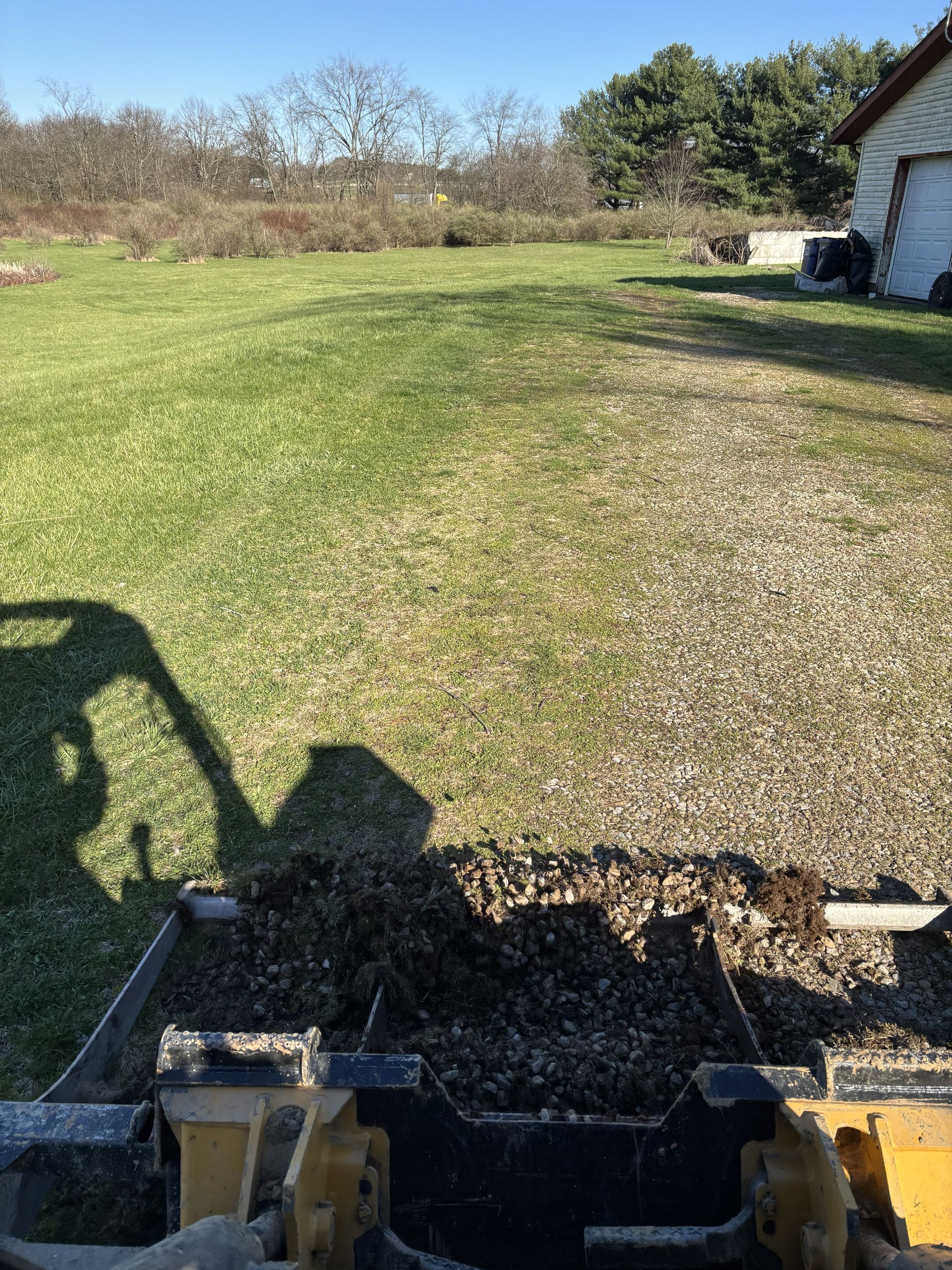 Grassy yard beside a white building, viewed from a tractor or mower in the foreground.