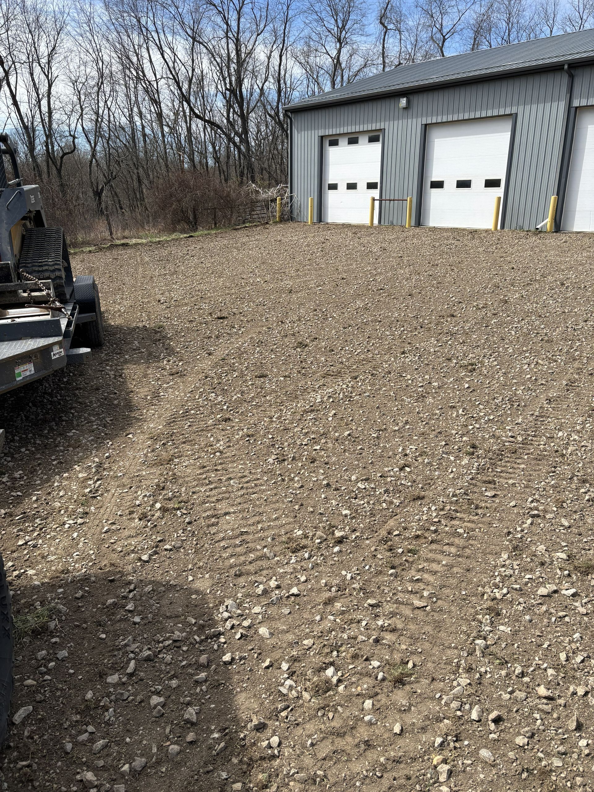Gravel pile beside a gray garage with two white doors, outdoors near bare trees