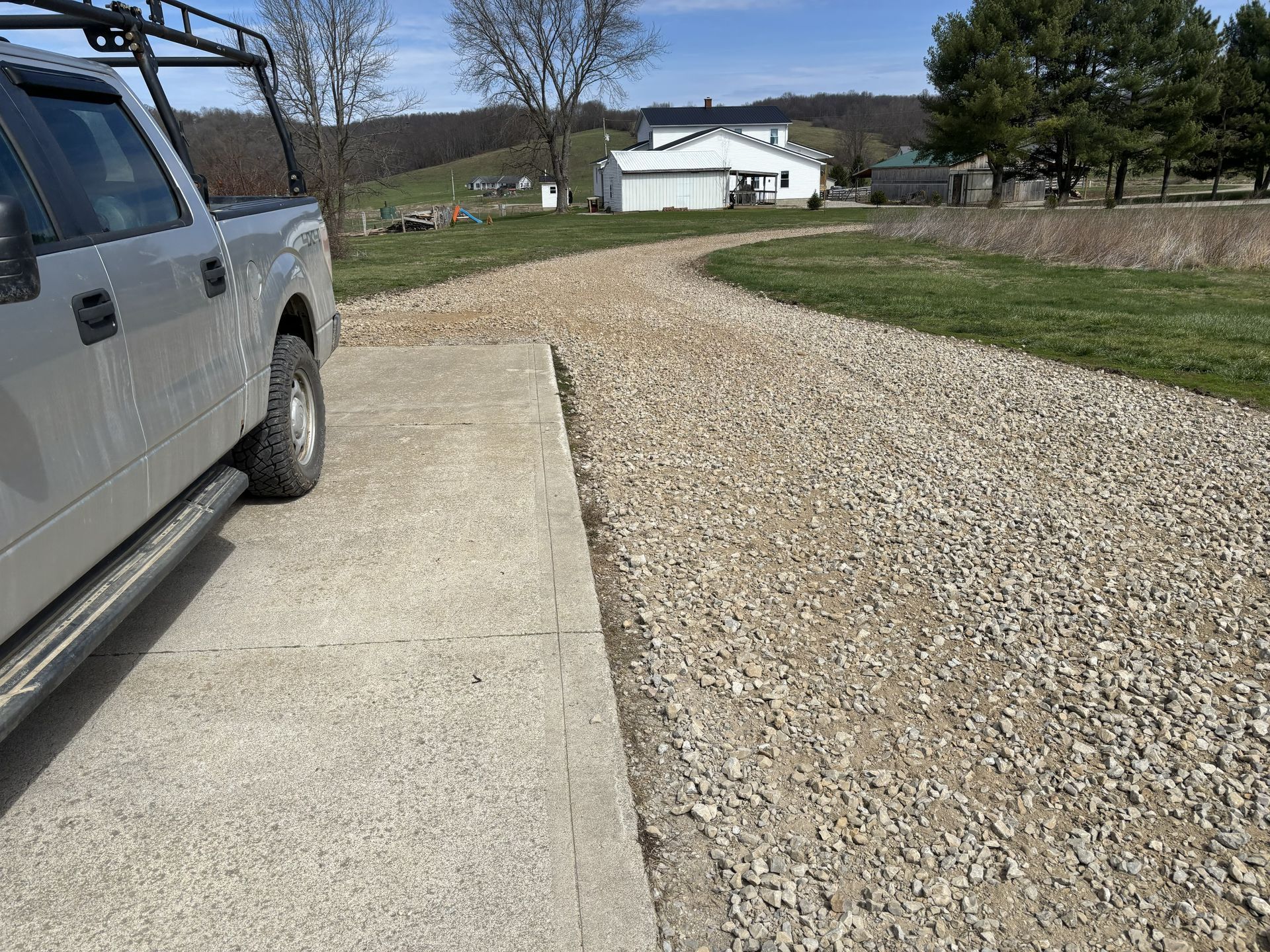 Gravel driveway beside a parked silver truck, leading to a white house in the distance.
