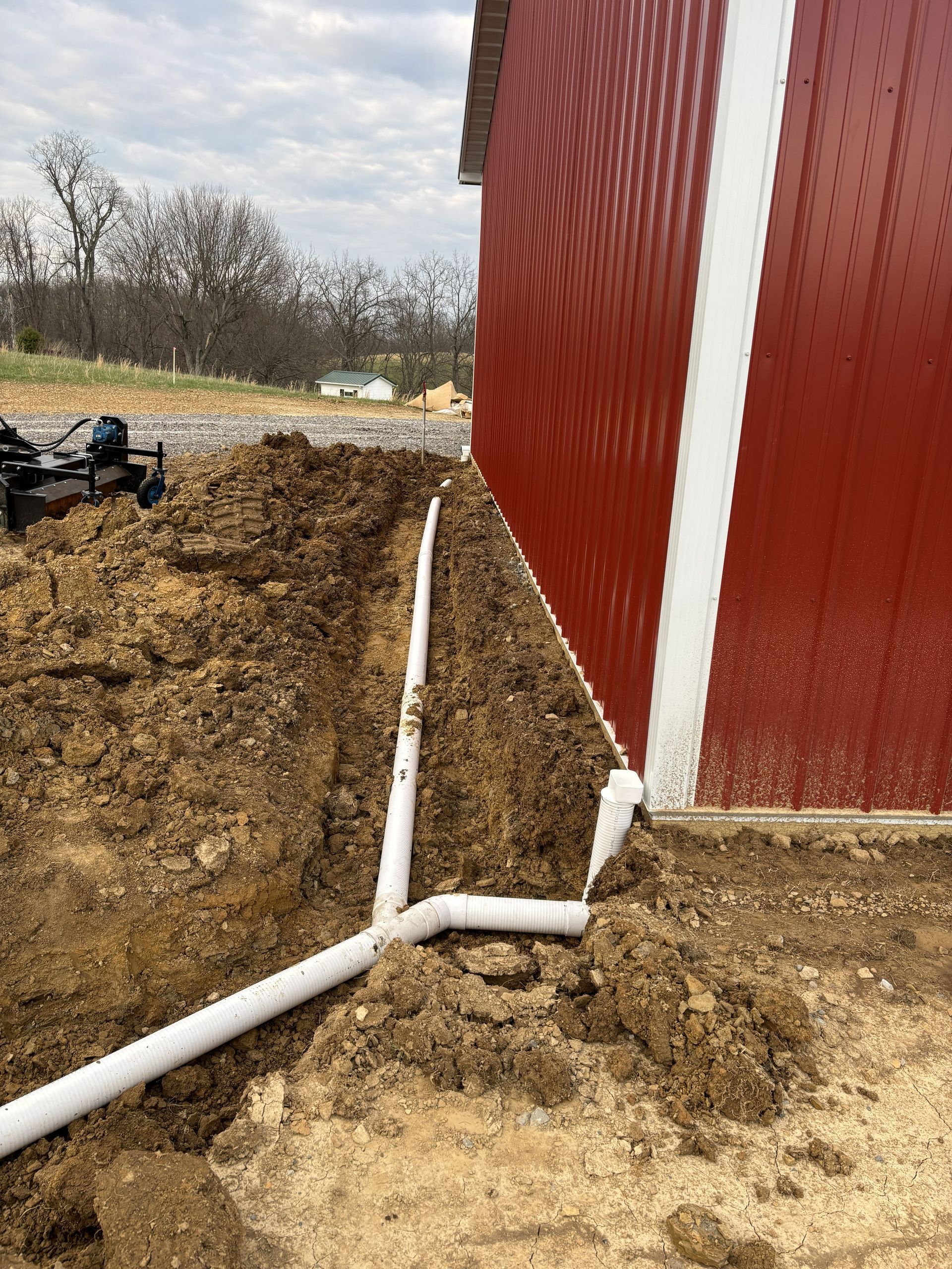 White drainage pipes along the base of a red building on a dirt construction site.
