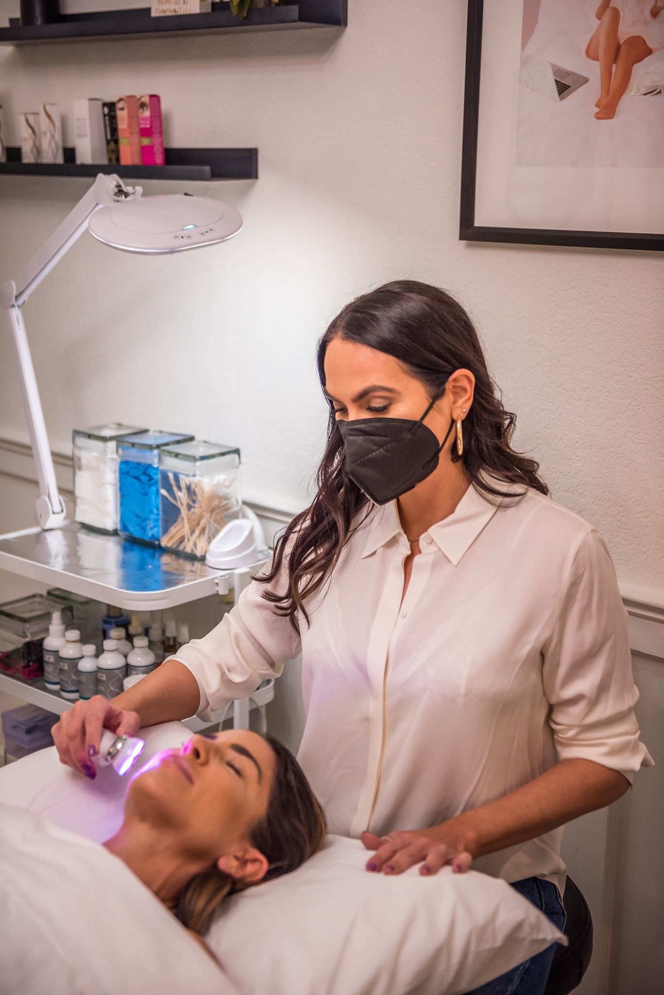 A woman wearing a mask is giving a woman a facial treatment.