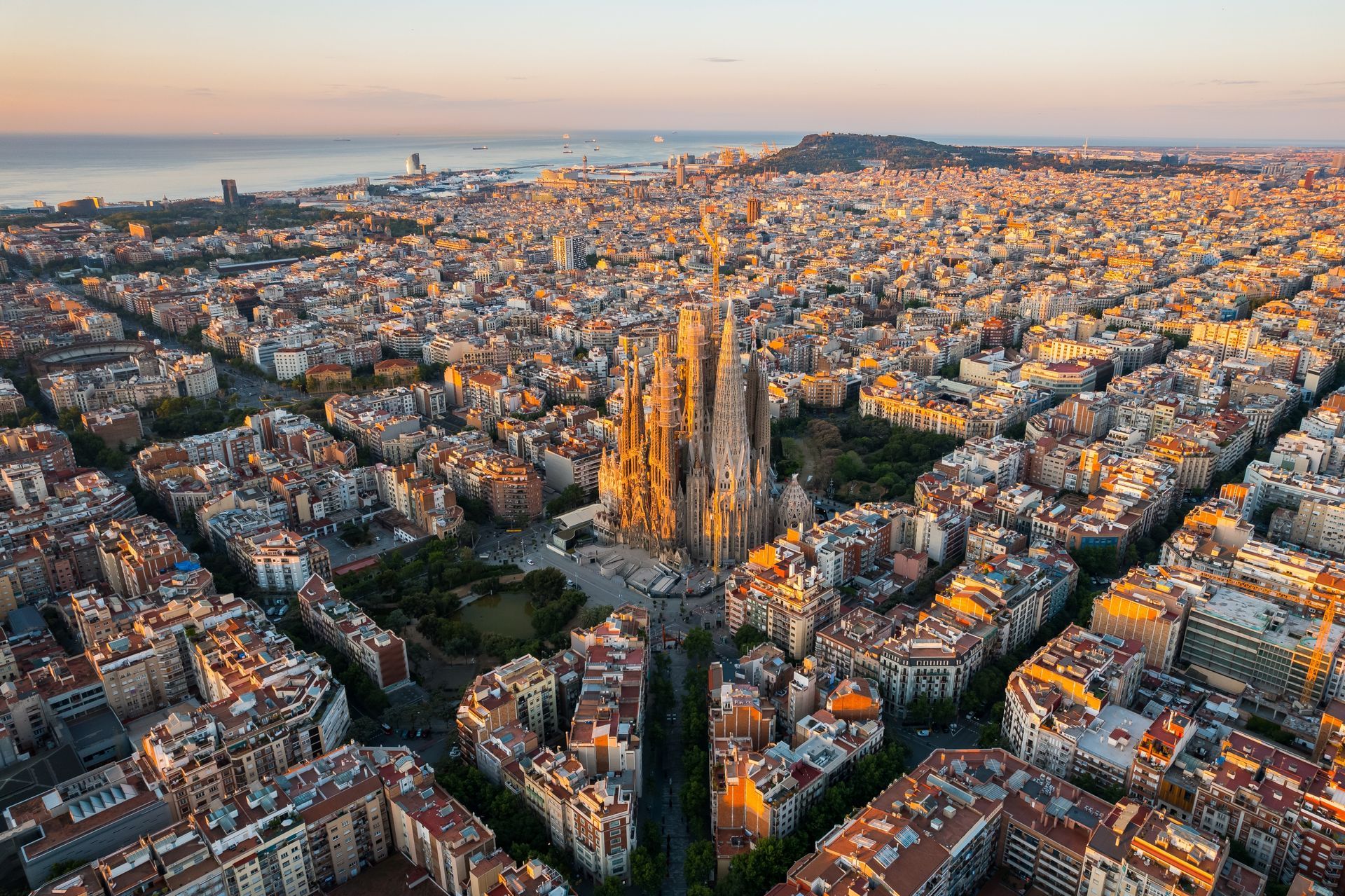 Aerial view of Barcelona at sunset, with the Sagrada FamÃlia rising above dense city blocks