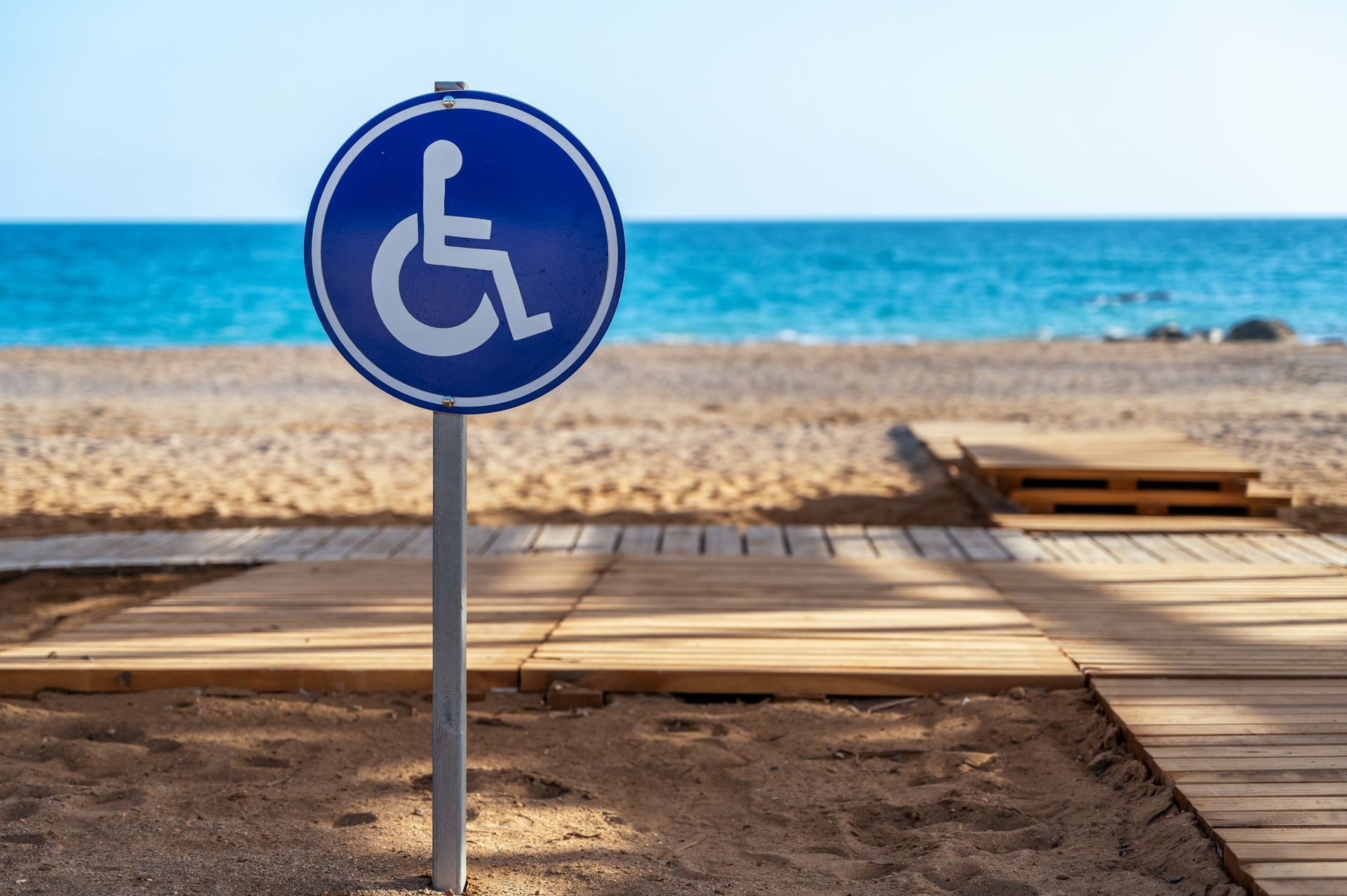 Accessible beach sign by wooden boardwalk with ocean in the background