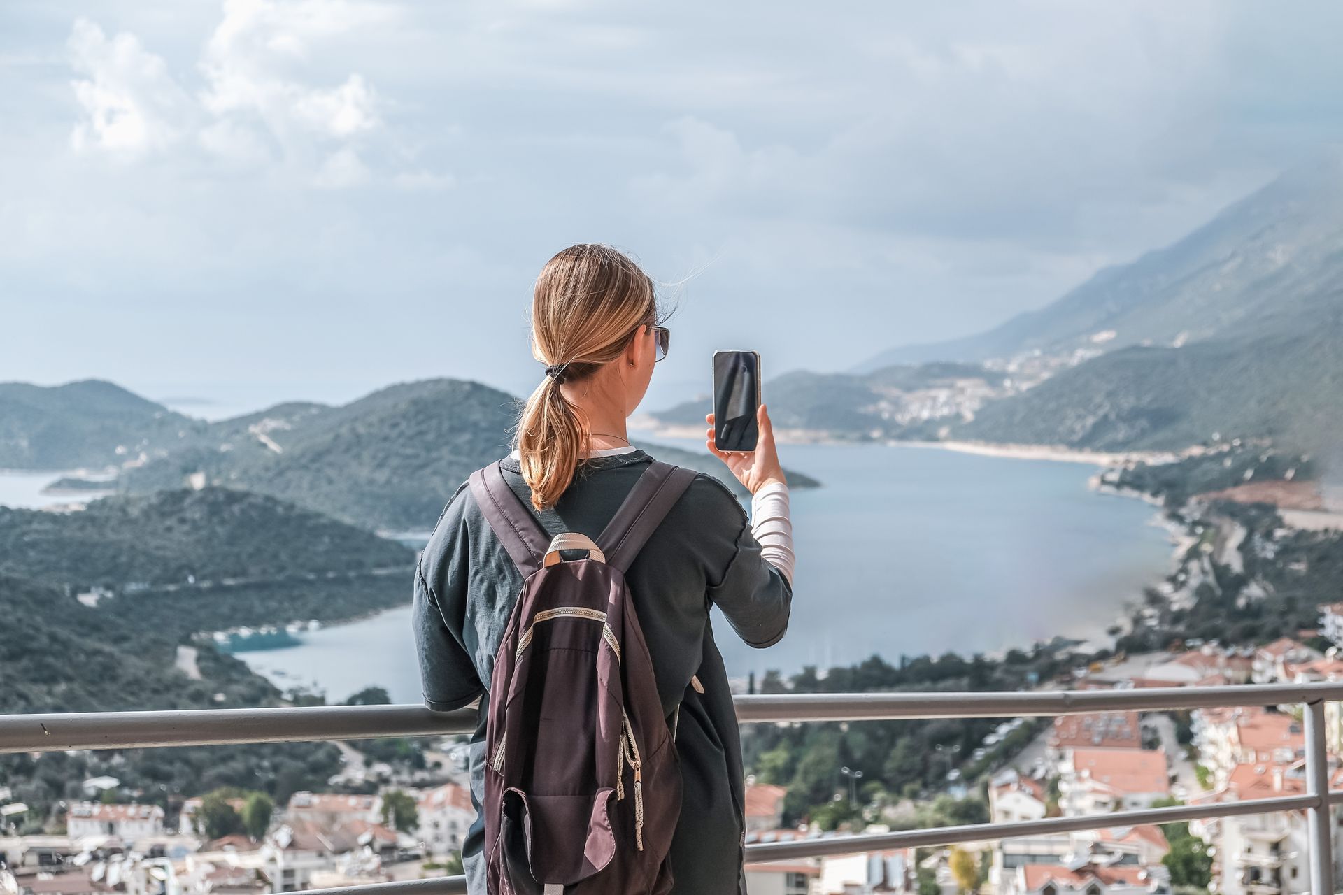 Person with backpack taking a photo of a coastal bay from a mountain lookout