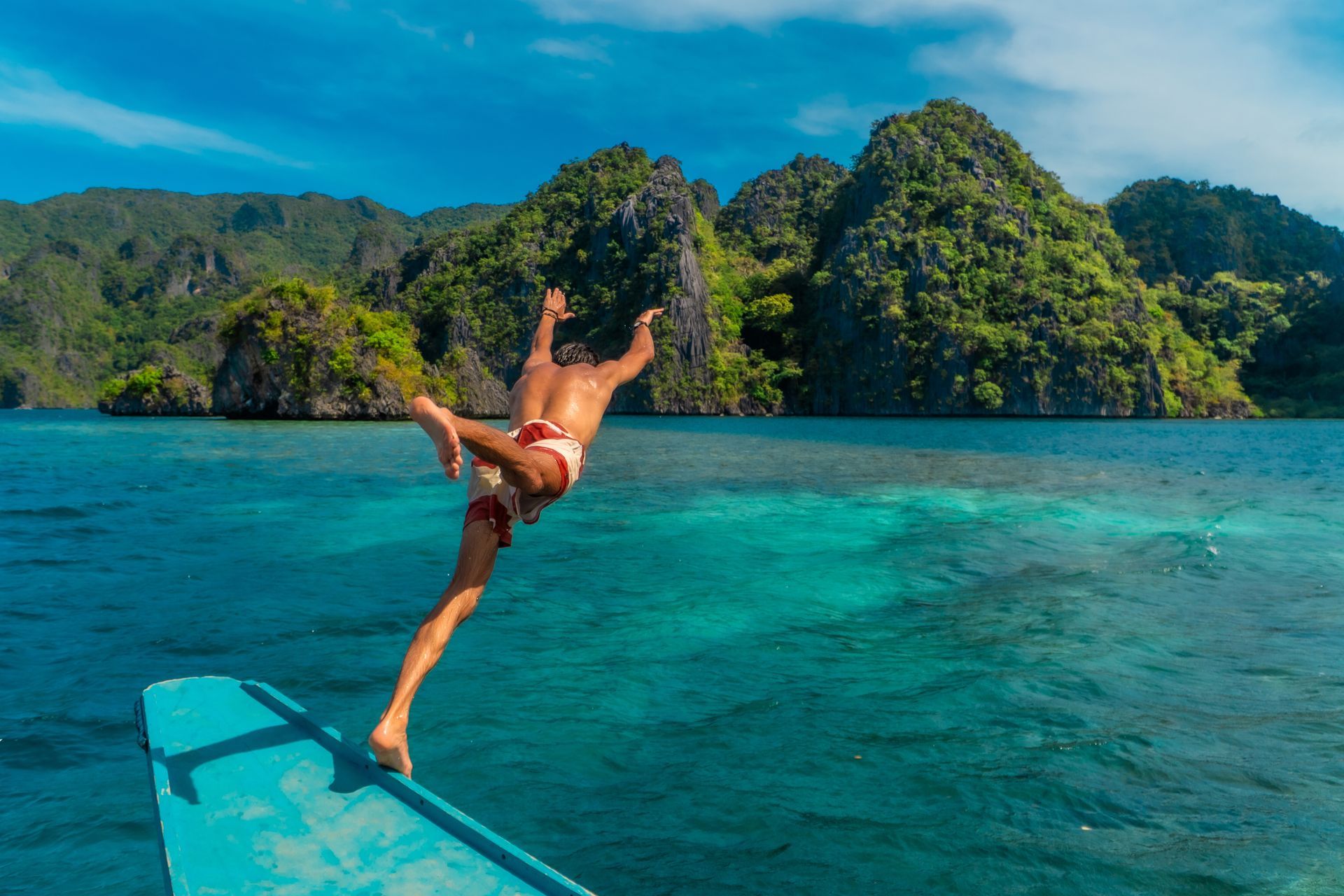 Person diving from a small boat into bright turquoise tropical water near lush green islands