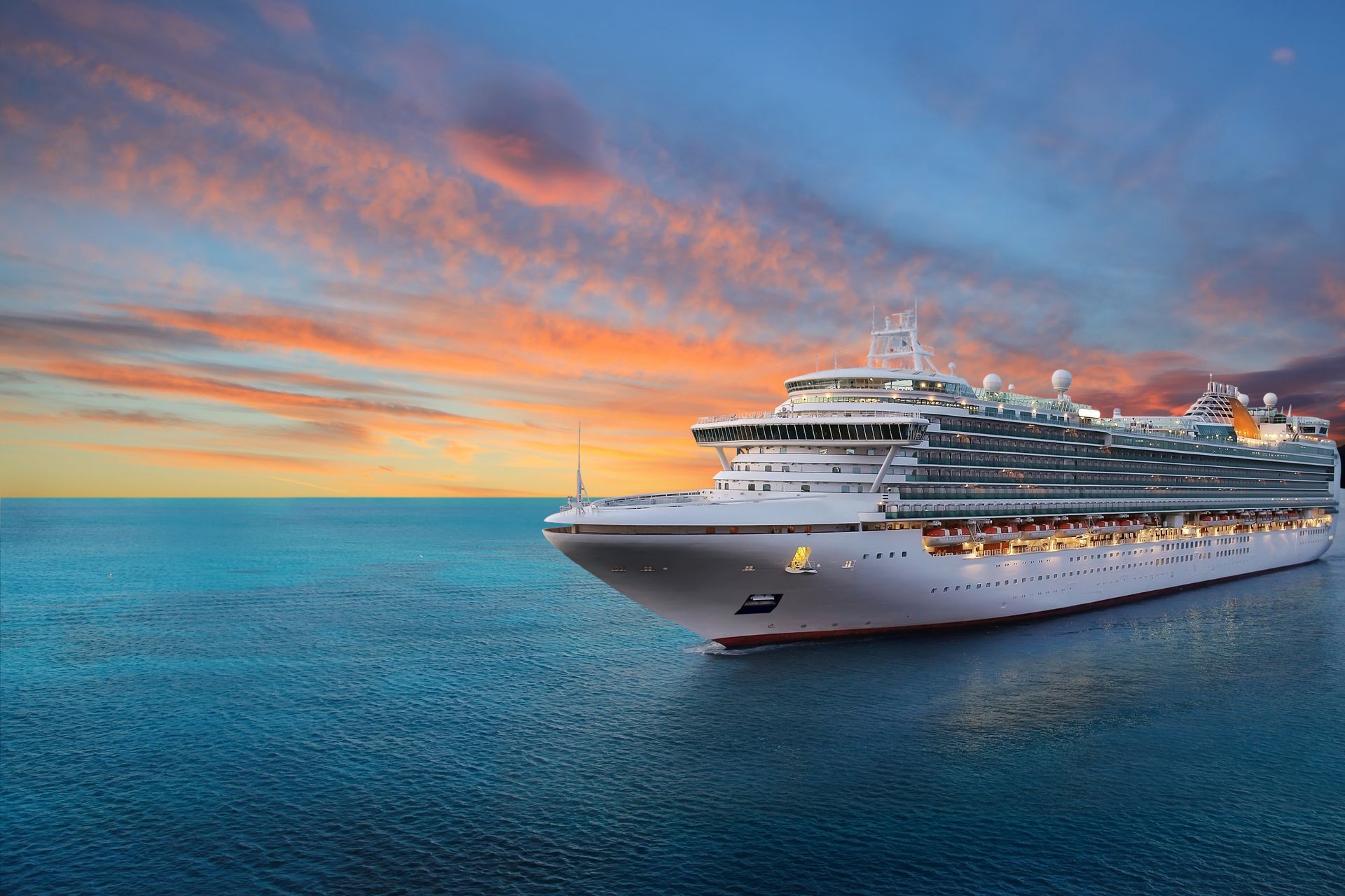 Large white cruise ship sailing on calm blue sea at sunset with colorful sky