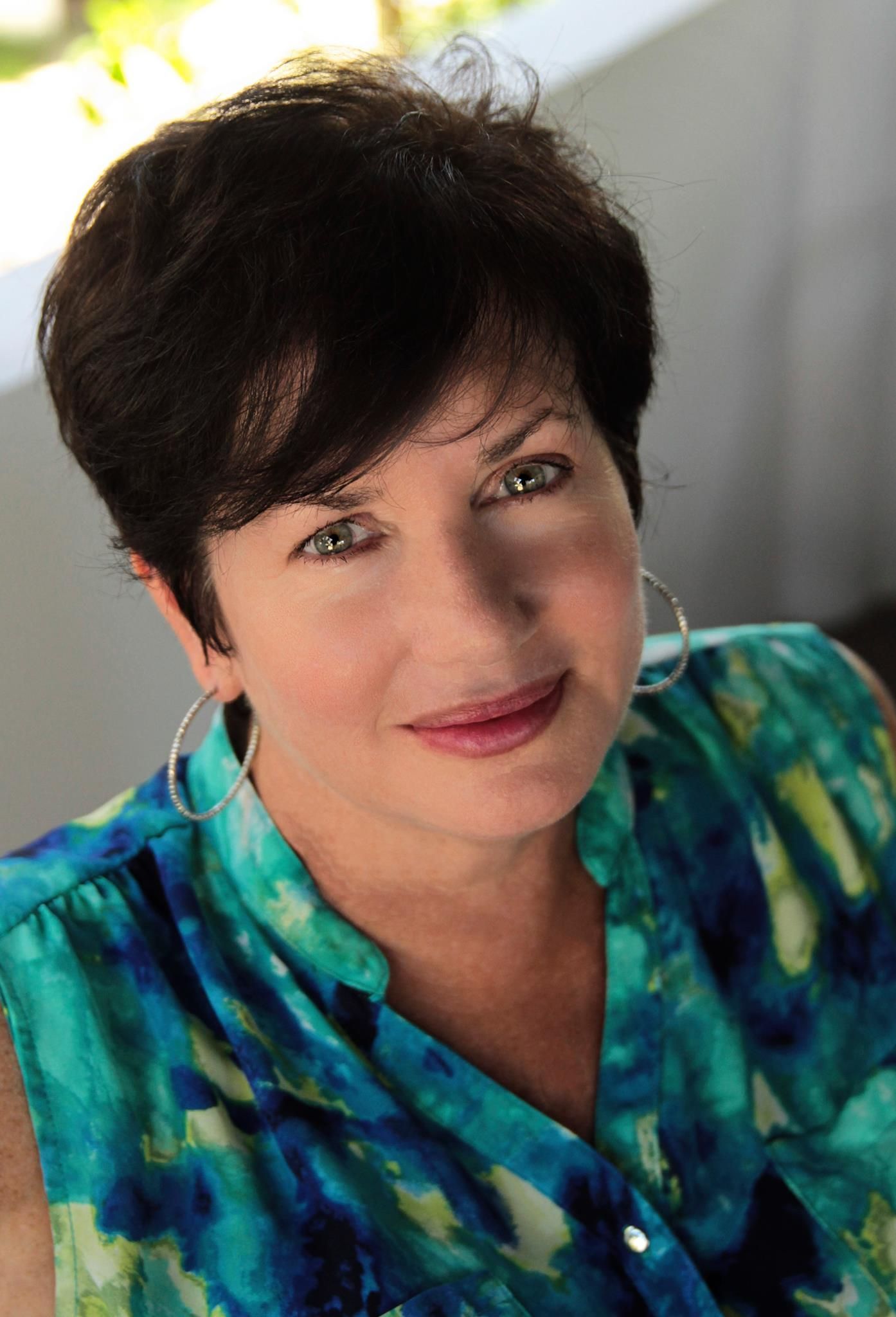 Woman with short dark hair and hoop earrings smiles, wearing a turquoise top.