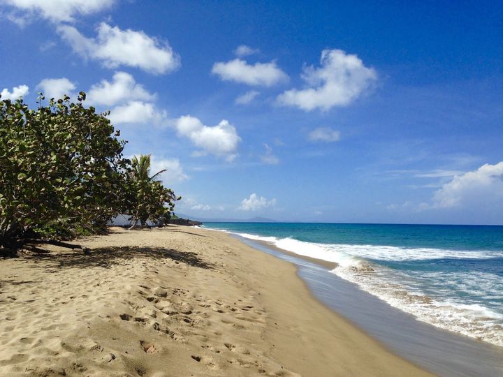 Sandy beach with turquoise water and blue sky with clouds.