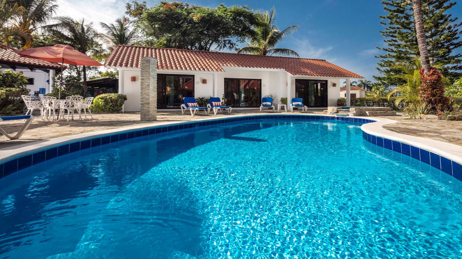 Swimming pool in front of a white, single-story triplex with a terracotta roof under a blue sky.