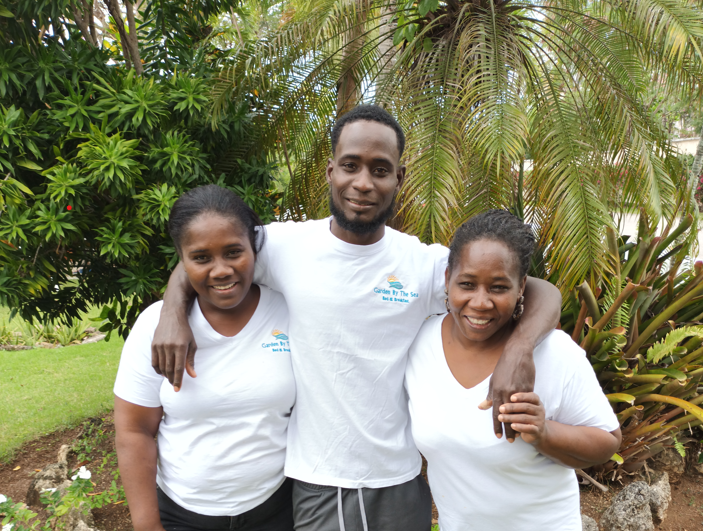 Three people smiling, posing outdoors. All wearing white shirts, trees in background.