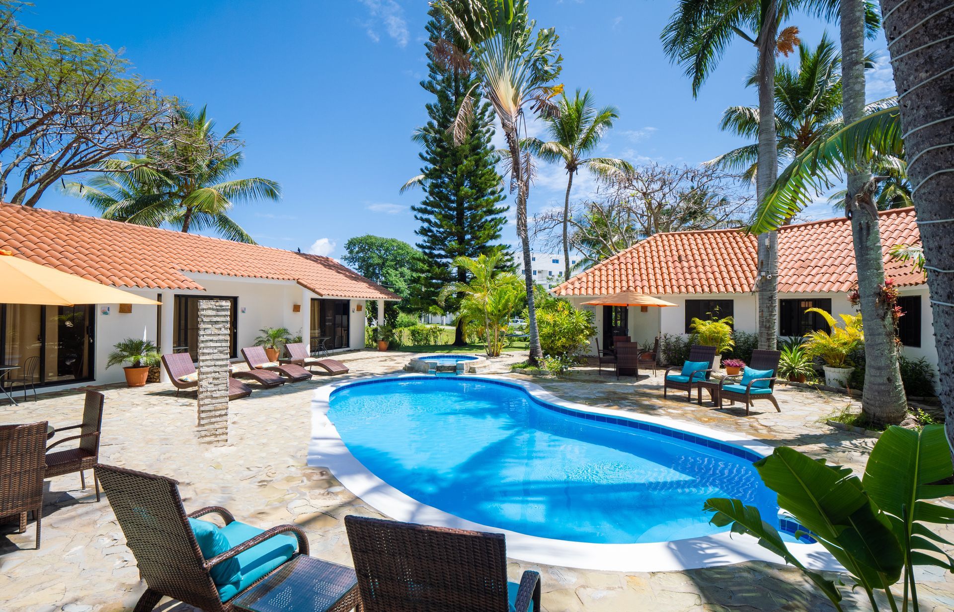 Pool surrounded by bungalows, palm trees, and lounge chairs under a bright blue sky.