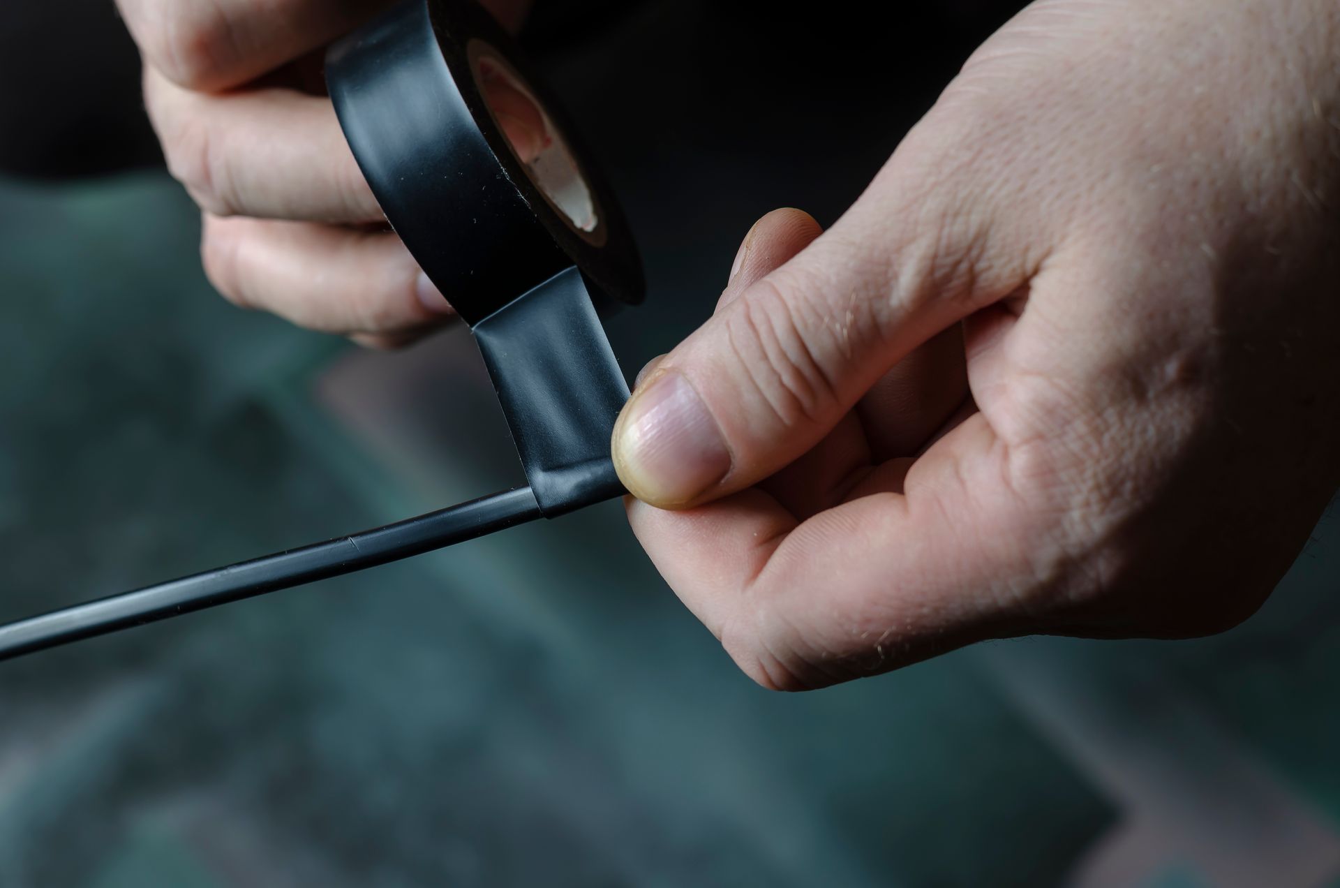 A close-up of hands applying black electrical tape to a thin black cable.